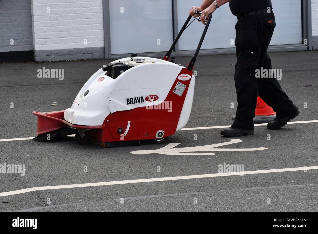 Ein Mann, der einen Weg auf einem Gehweg mit einer Handkehrmaschine reinigt Stockfoto