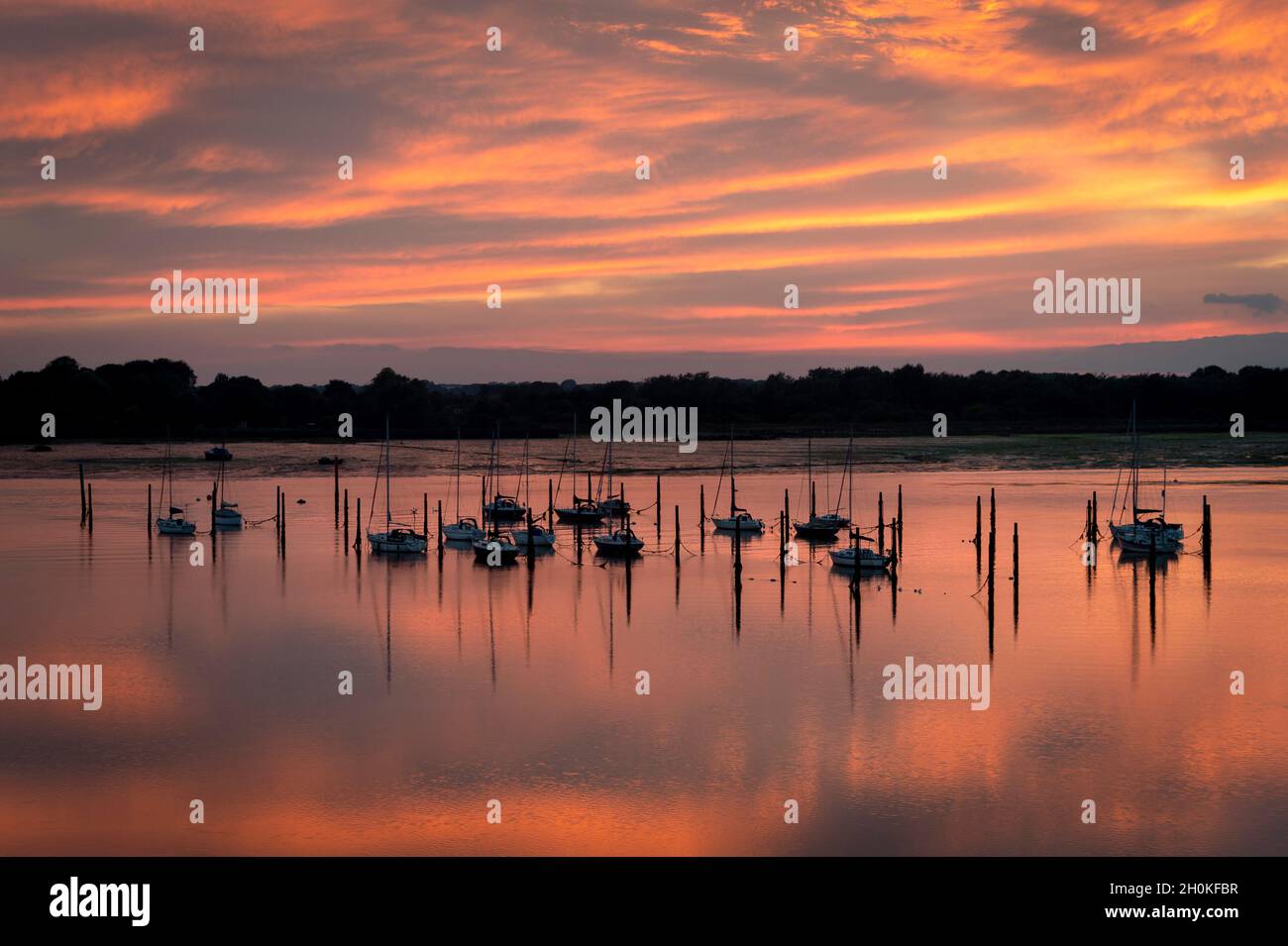 Boote, die auf Pilings in Portchester Reach in Portsmouth Harbour, Hampshire, Großbritannien, festgemacht sind. Sonnenuntergang mit dramatischem orangefarbenem Himmel. Stockfoto