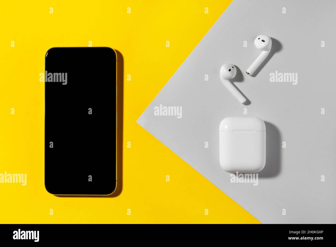 Smartphone und kabellose Kopfhörer auf gelbem und grauem Hintergrund. Stockfoto