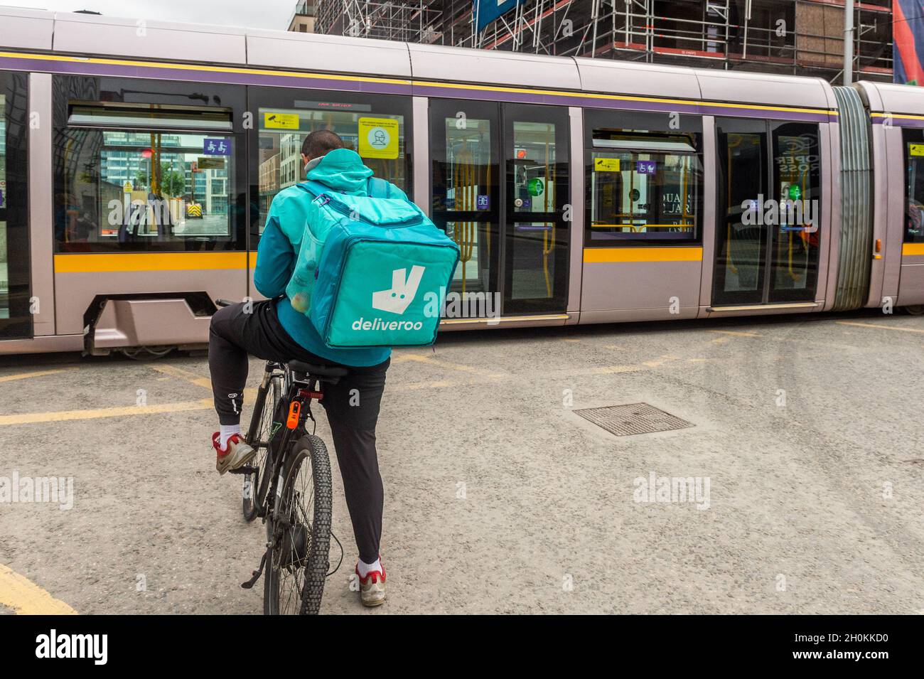 Deliveroo-Fahrer wartet auf eine LUAS-Straßenbahn, Dublin, Irland. Stockfoto