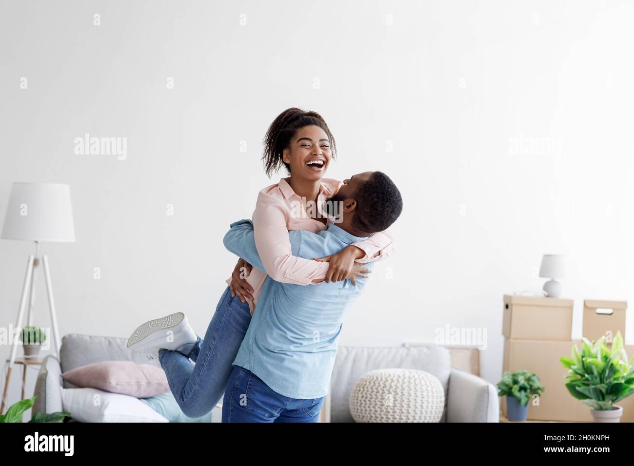Glückliches Paar, das bei gekauftem Haus umzieht, hebt Ehemann geliebte Frau auf, Familie beginnt neues Leben bei der ersten Wohnung Stockfoto