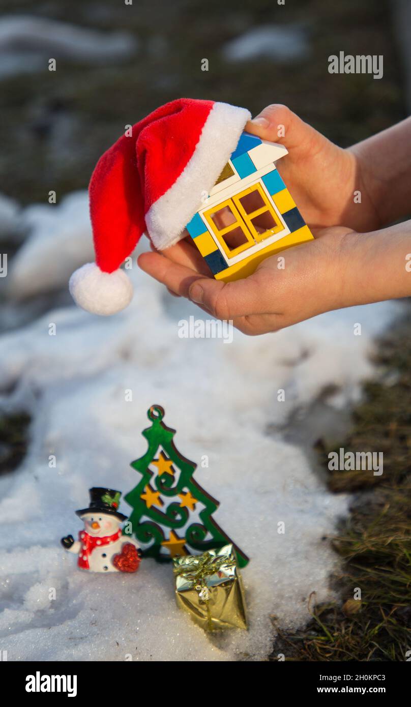 Kinderhände halten ein kleines Haus aus Bauwerk in Santa Hut. Träume von einem neuen Zuhause, Kinderfantasien über ein fabelhaftes Geschenk. Neues ho Stockfoto