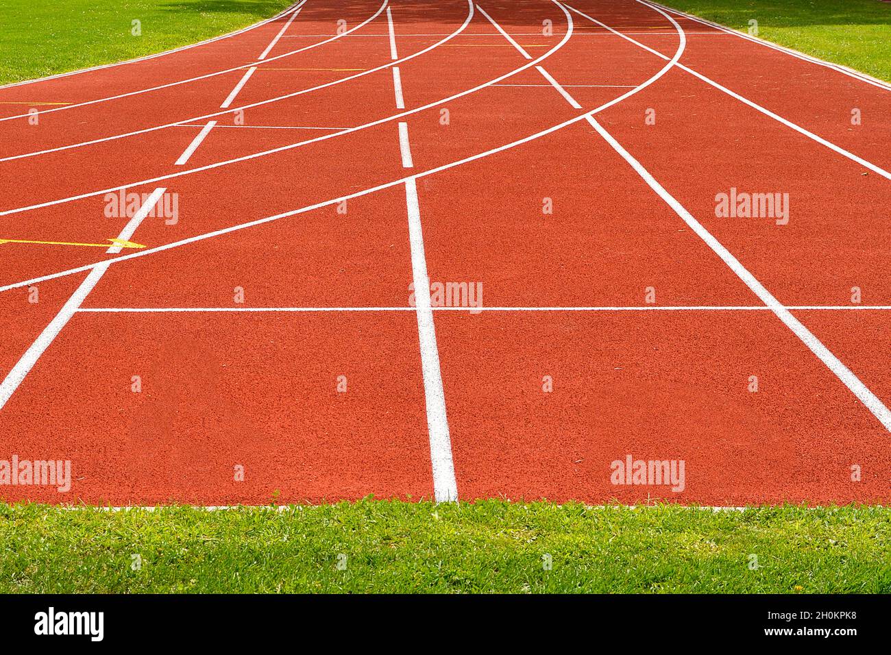 Die schartanne Leichtathletik-Strecke beginnt mit Gras um sie herum und mehreren Bahnen Stockfoto