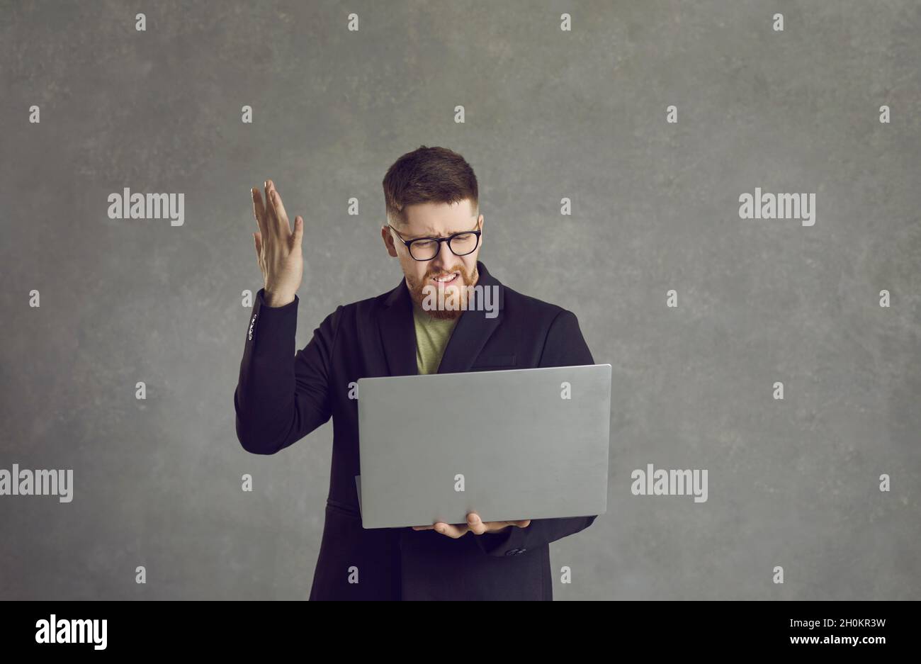 Wütender und frustrierter kaukasischer Mann, der Stress erlebt, winkt mit der Hand, während er einen Laptop hält. Stockfoto
