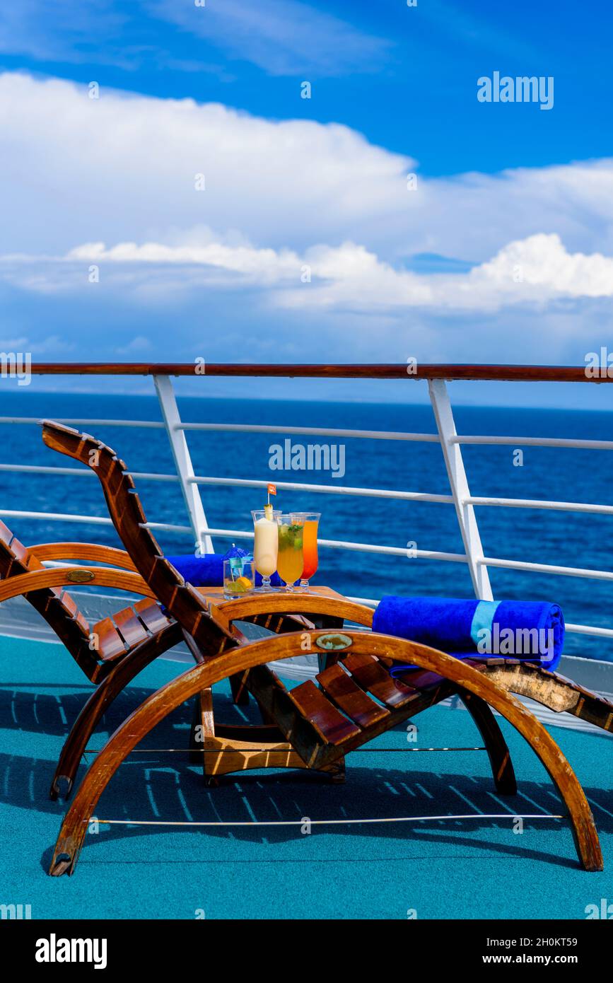 Sonnenliegen, um den Blick auf das Meer zu genießen, mit einem Cocktailtisch daneben auf dem Schiffsdeck. Stockfoto