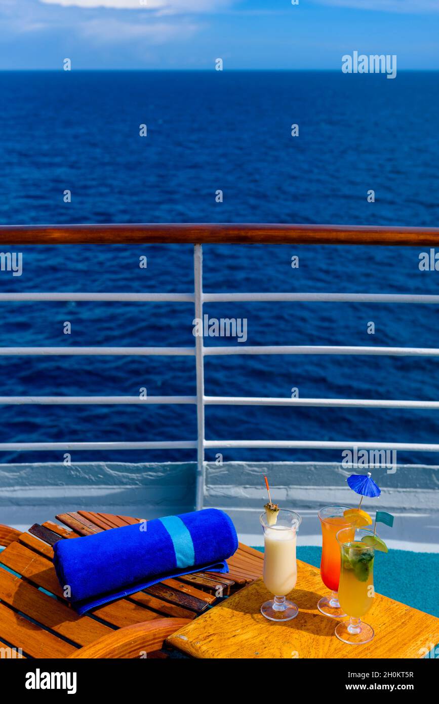 Sonnenliegen, um den Blick auf das Meer zu genießen, mit einem Cocktailtisch daneben auf dem Schiffsdeck. Stockfoto