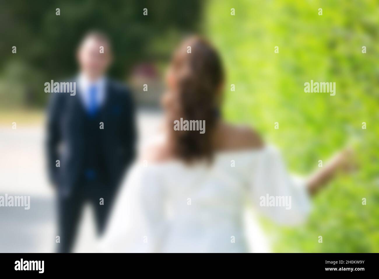 Der Bräutigam in einer strengen Jacke wartet auf seine Braut, die ihm entlang der grünen Büsche entgegengeht. Kein Fokus, verschwommen, Stockfoto