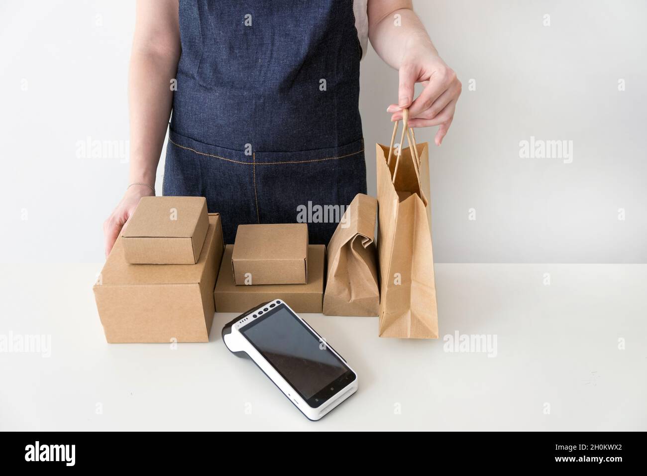 Frau Unternehmerin trägt blaue Denim Schürze geben die Kraftpapier Tasche mit einem Auftrag an einen Kunden Stockfoto