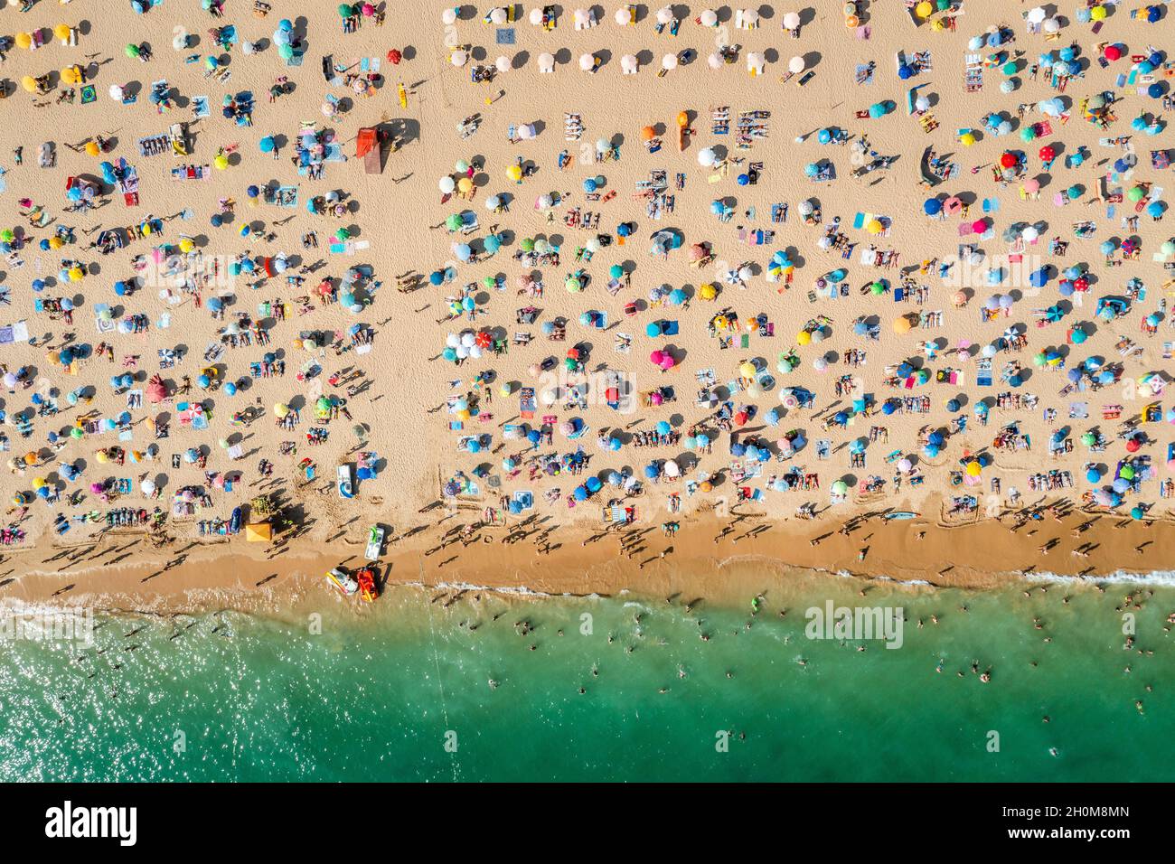 Drohnenaufnahme von vielen Menschen, die den Strand und das Meer genießen - Urlaubsmuster. Rocha Beach in Portimao, Portugal Stockfoto