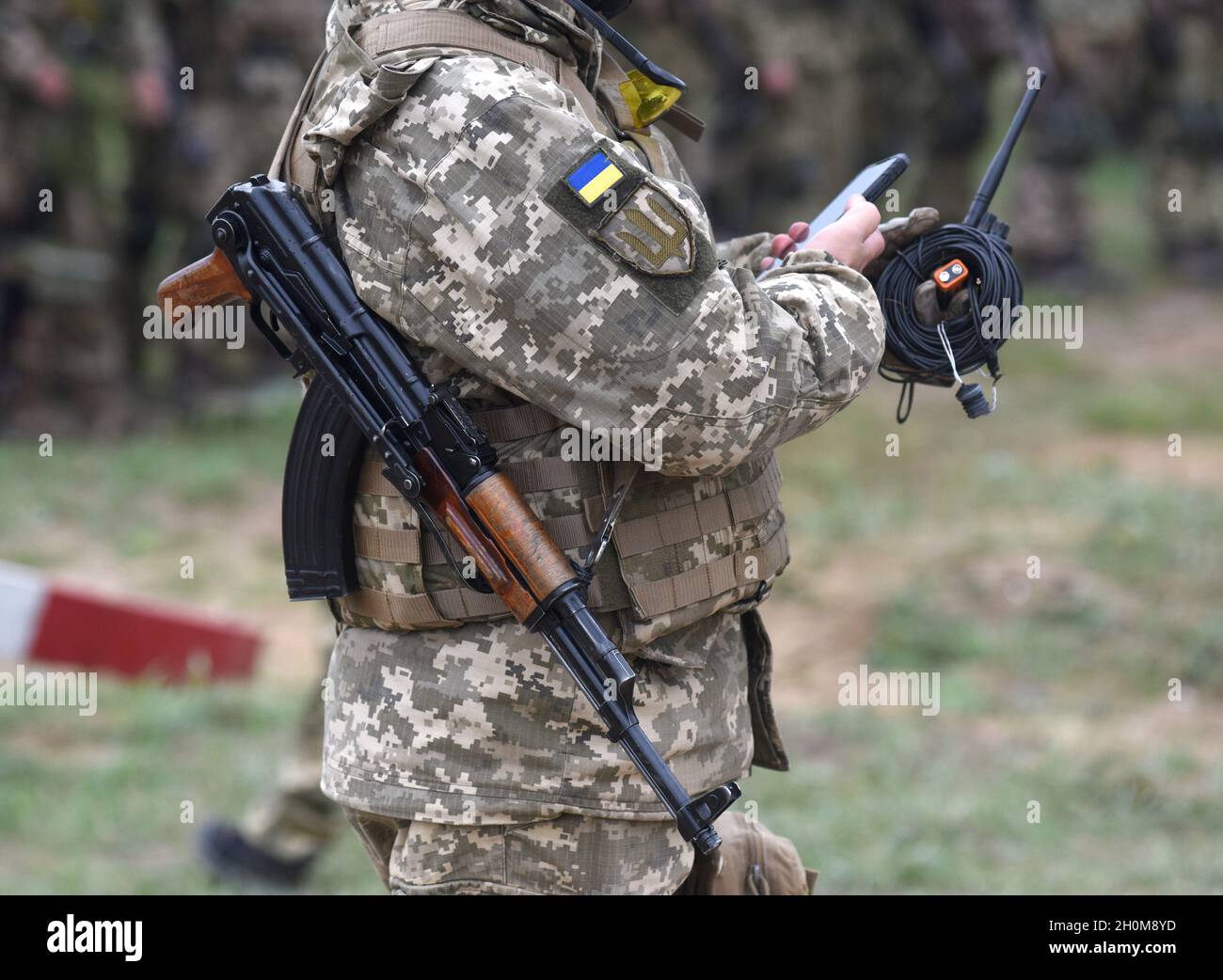 Soldat der Ukraine mit Sturmgewehr AK Smartphone verwenden. Ukrainischer Soldat mit Sturmgewehr AK. Stockfoto