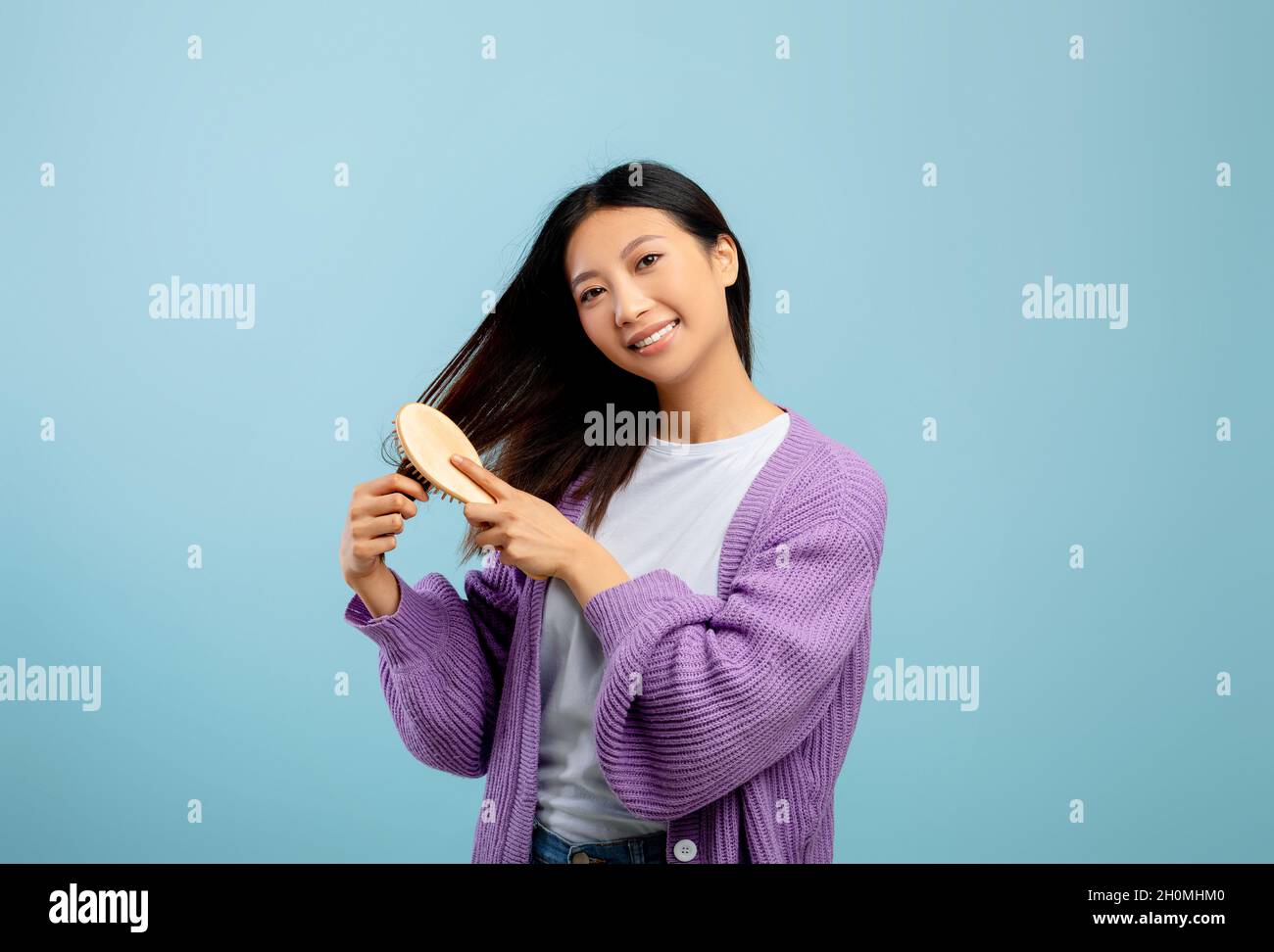 Haarpflege und Beauty-Konzept. Glückliche junge asiatische Dame, die ihr natürliches, dunkles, seidiges Haar mit Holzkamm putzt Stockfoto