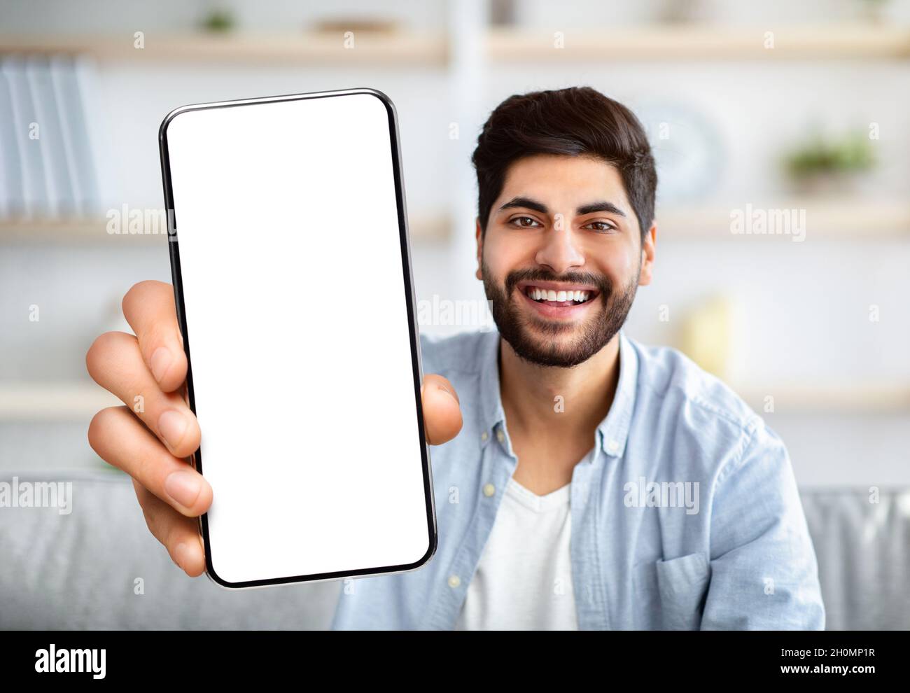 Fröhlicher Arabischer Mann Zeigt Smartphone Mit Großem Weißen Bildschirm An Der Kamera Stockfoto