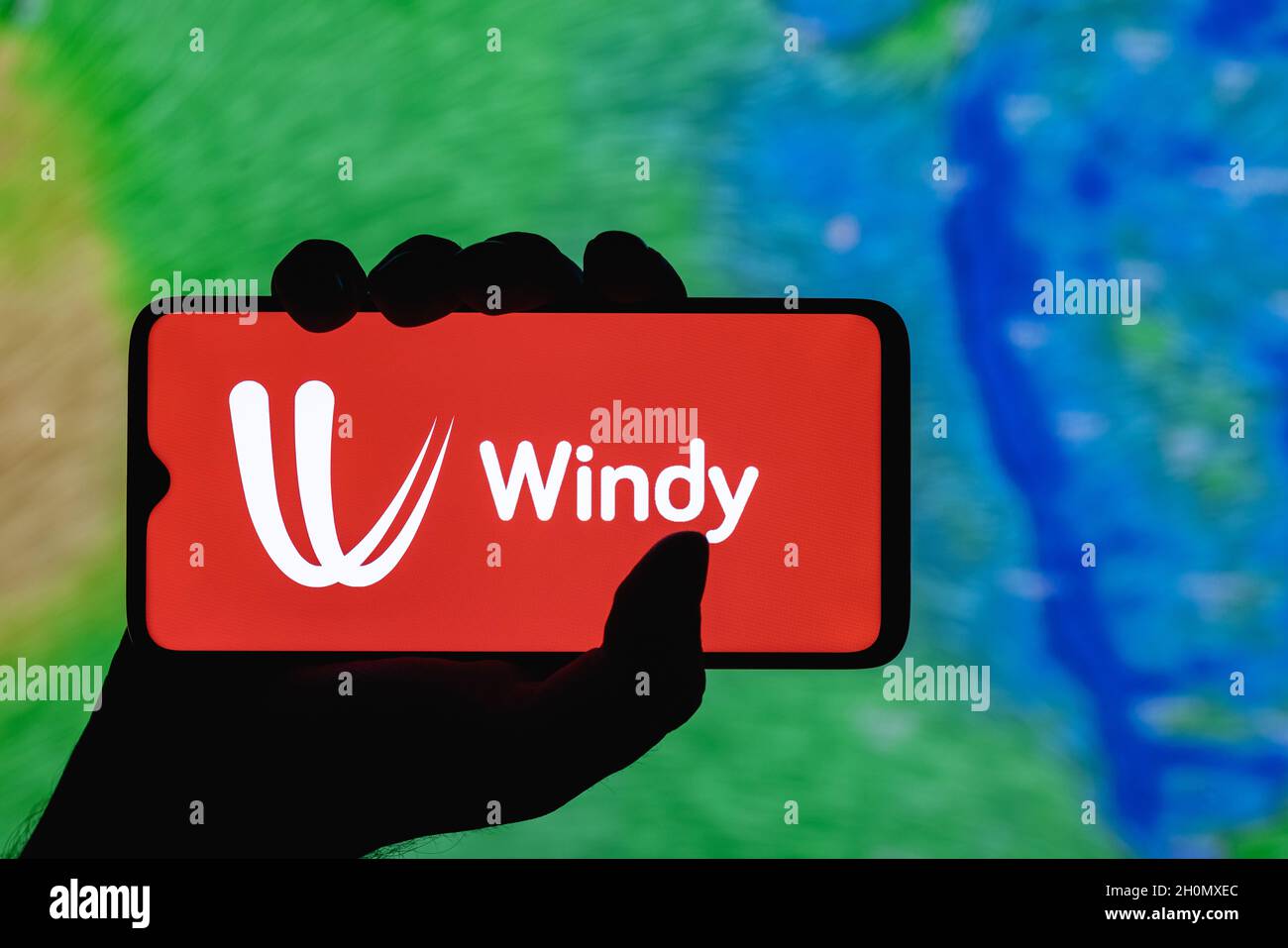 Windy ist ein interaktiver Wetterprognosedienst weltweit. Windiges Logo auf dem Smartphone-Bildschirm. Auf dem Hintergrund der Wettervorhersage über Indien. Stockfoto