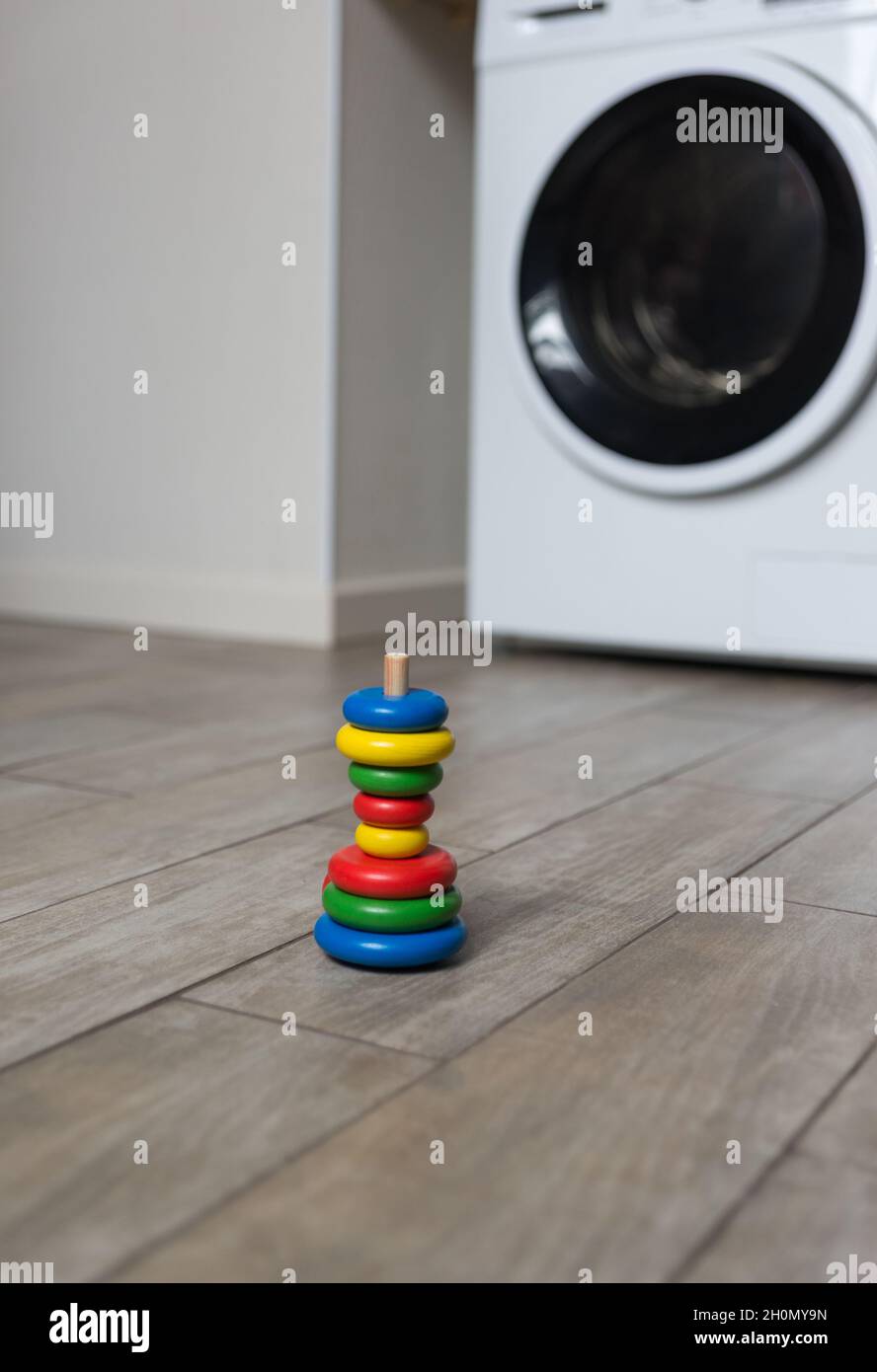 Eine falsch montierte mehrfarbige Kinderpyramide steht auf dem Boden in der Waschküche vor dem Hintergrund einer Waschmaschine Stockfoto