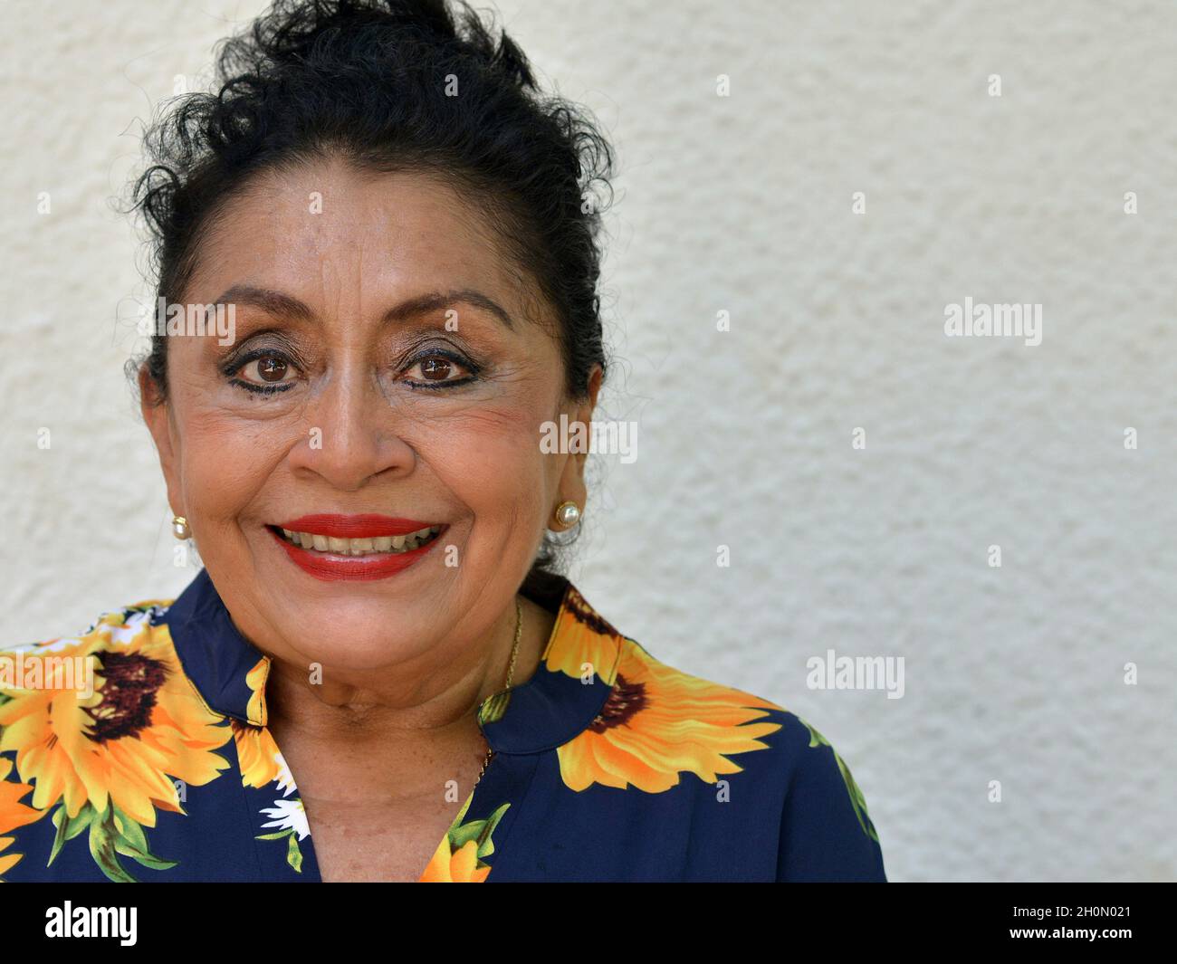 Ältere, optimistische, positive, selbstbewusste, mexikanisch-kaukasische Latina-Frau mit Make-up lächelt und schaut den Betrachter vor grauem Hintergrund an. Stockfoto