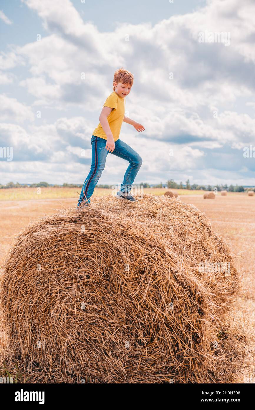 Der rothaarige kaukasische Junge geht auf einem Farmfeld unter Heuhaufen - Weitwinkel und offene Öffnung Stockfoto