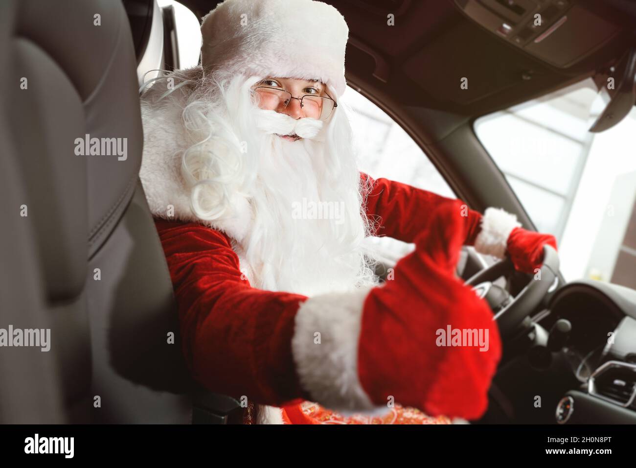 Der Weihnachtsmann, der hinter dem Steuer eines Autos sitzt, zeigt einen Daumen nach oben - ein Klassenschild. Stockfoto