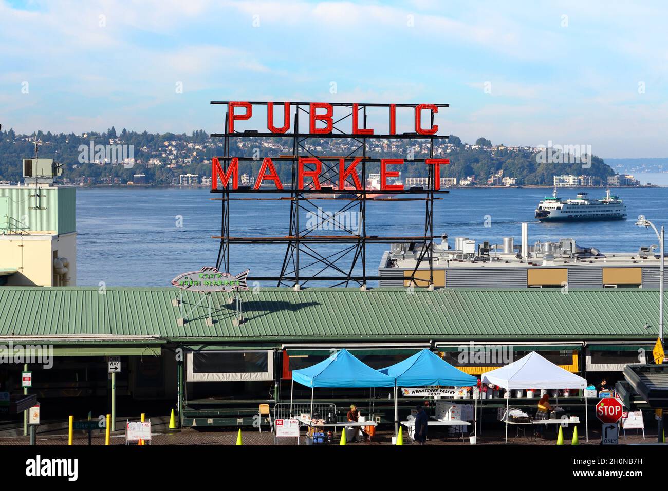 Blick auf den Pike Place Market und das Neonschild des öffentlichen Marktes mit Puget Sound, dem Viertel North Admiral und einer Washington State Ferry im Hintergrund. Stockfoto