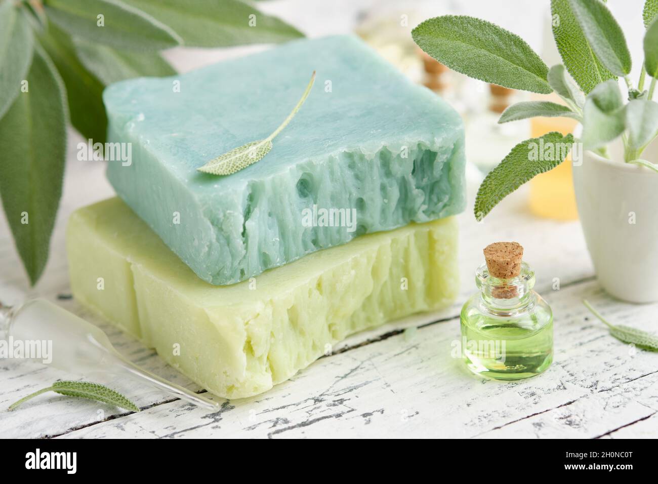 Hausgemachte natürliche Bio-Seifenstücke, eine Flasche ätherisches Salbeiöl und frische grüne Salbeiblätter auf dem weißen Holztisch. Stockfoto