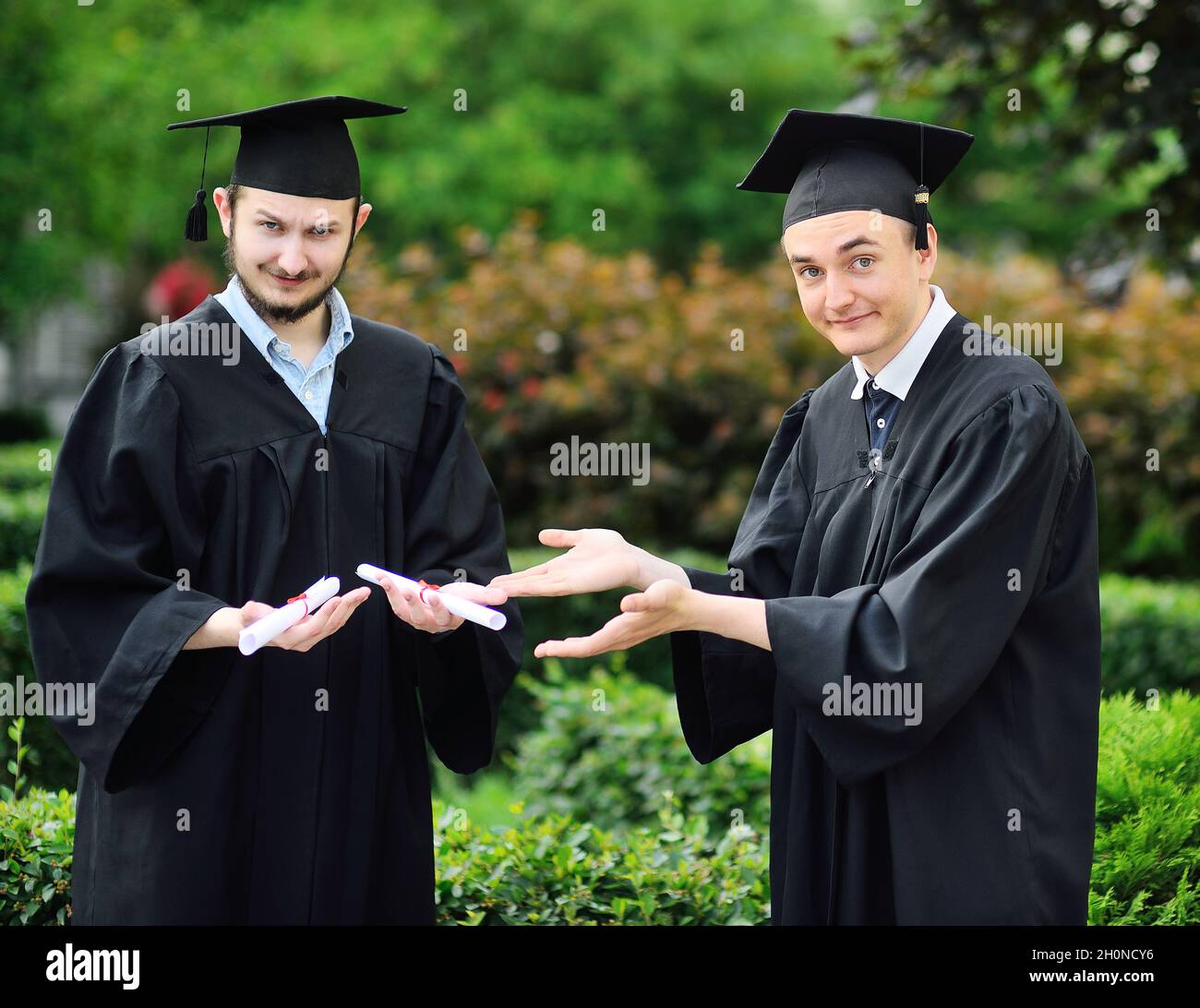 Zwei junge Hochschulabsolventen in Gewändern und quadratischen Hüten freuen sich über ein Diplom. Stockfoto