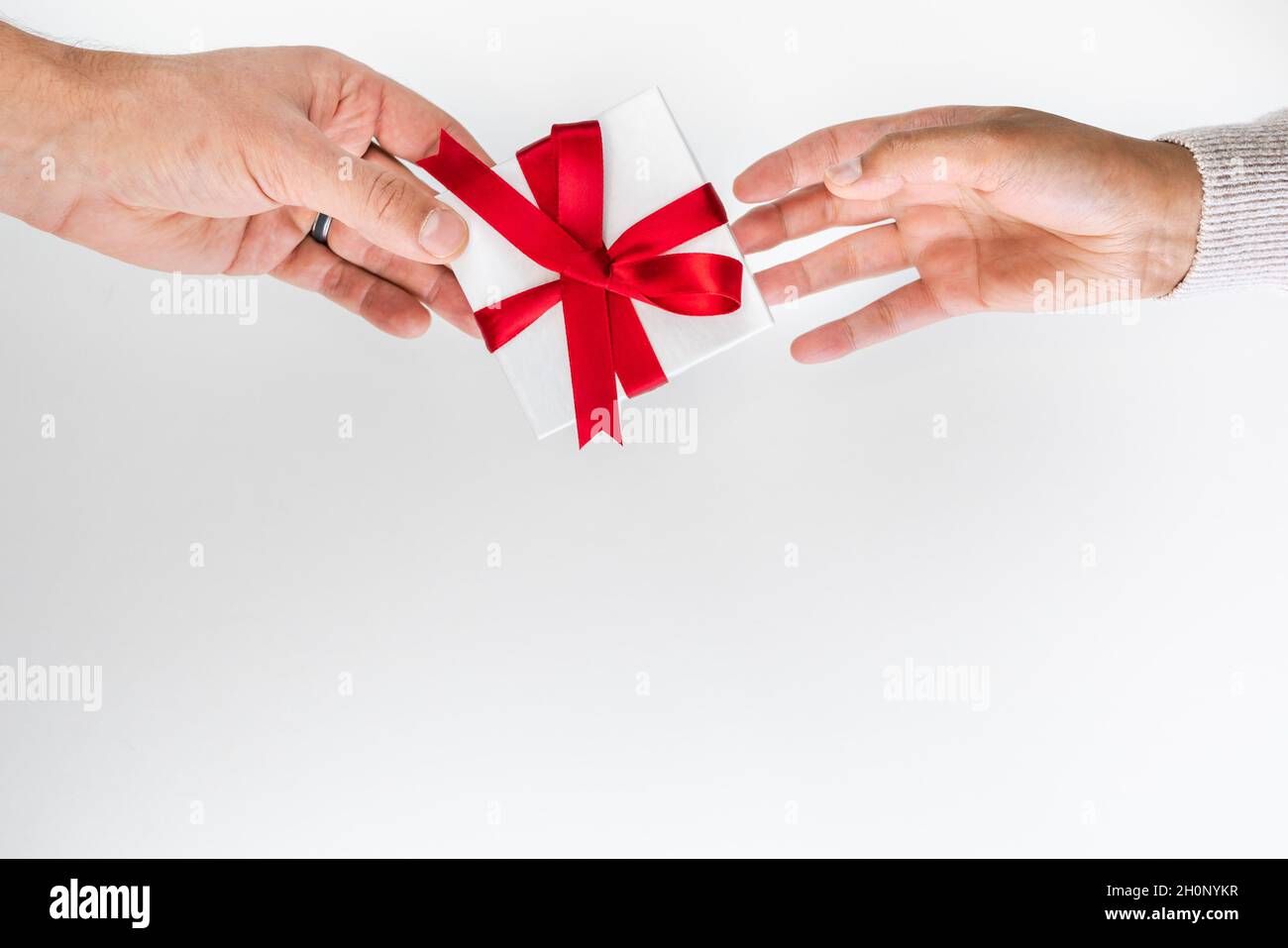 Schöne Feiertage oder Weihnachten Hintergrundbild eines kaukasischen männlichen Hand geben eine kleine rote Band verpackt Geschenkbox an eine gemischte Rasse Afroamerikaner Stockfoto