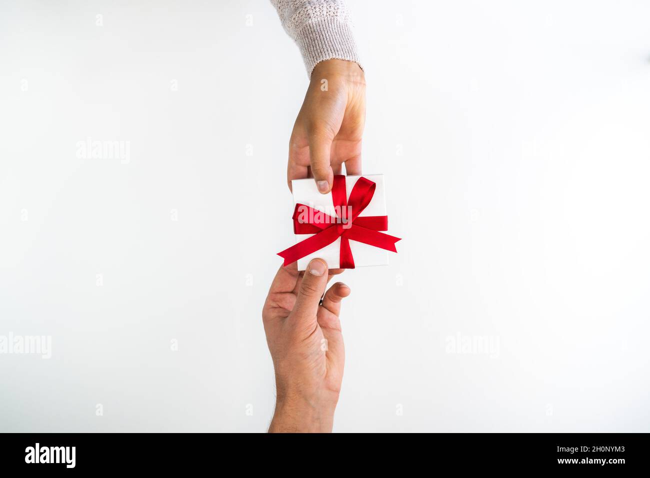 Schöner Urlaub oder Weihnachten Hintergrundbild der Hände eines kaukasischen Mannes und Mischling Rasse Frau Austausch eines kleinen roten Band verpackt weißes Geschenk Stockfoto