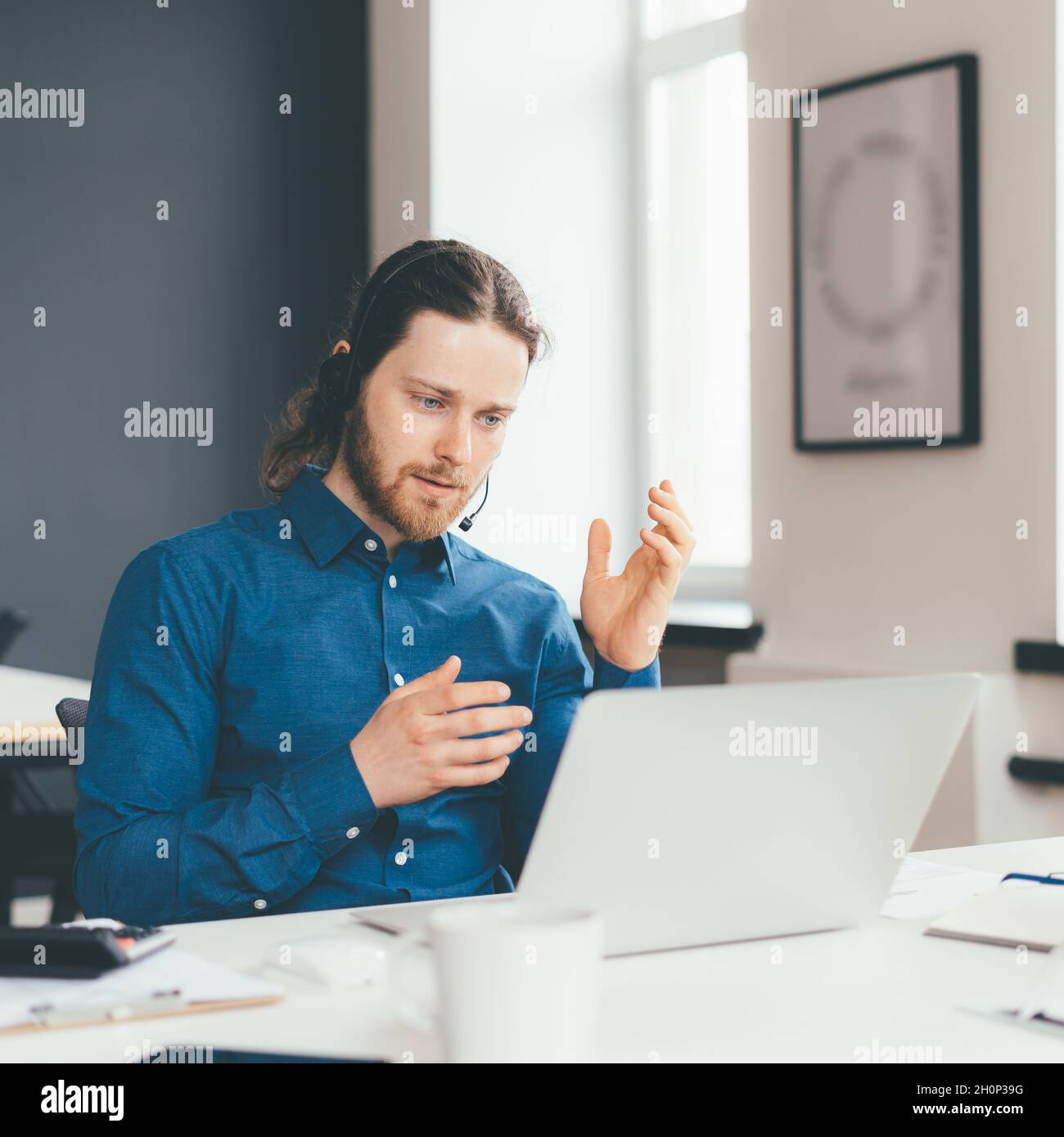 Konzentrierter junger Mann in Headset und Freizeitkleidung im Gespräch mit dem Kunden auf dem Laptop im Büro Stockfoto