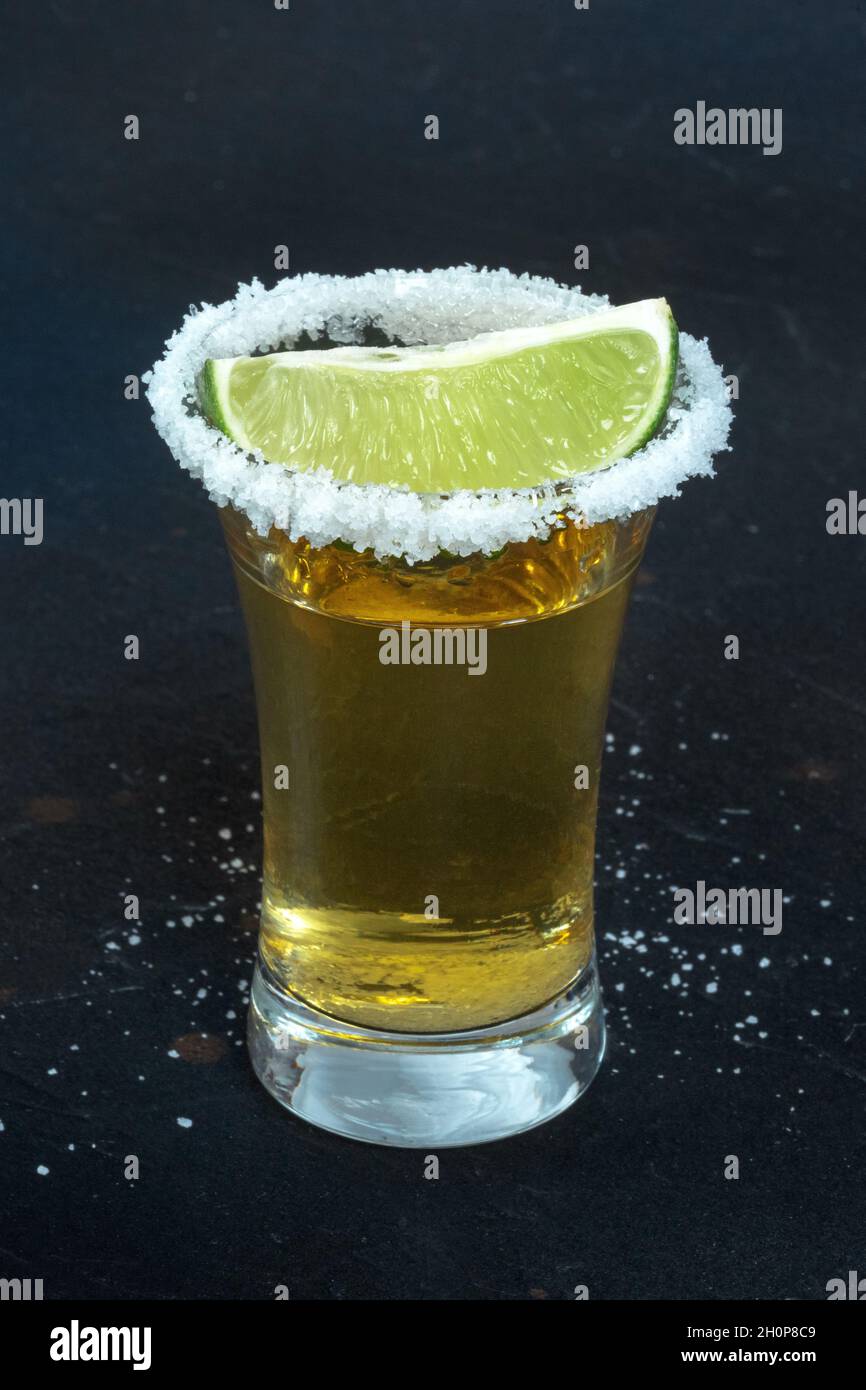 Tequila Schuss, mit einem gesalzenen Rand und einer Limettenscheibe, auf schwarzem Hintergrund Stockfoto