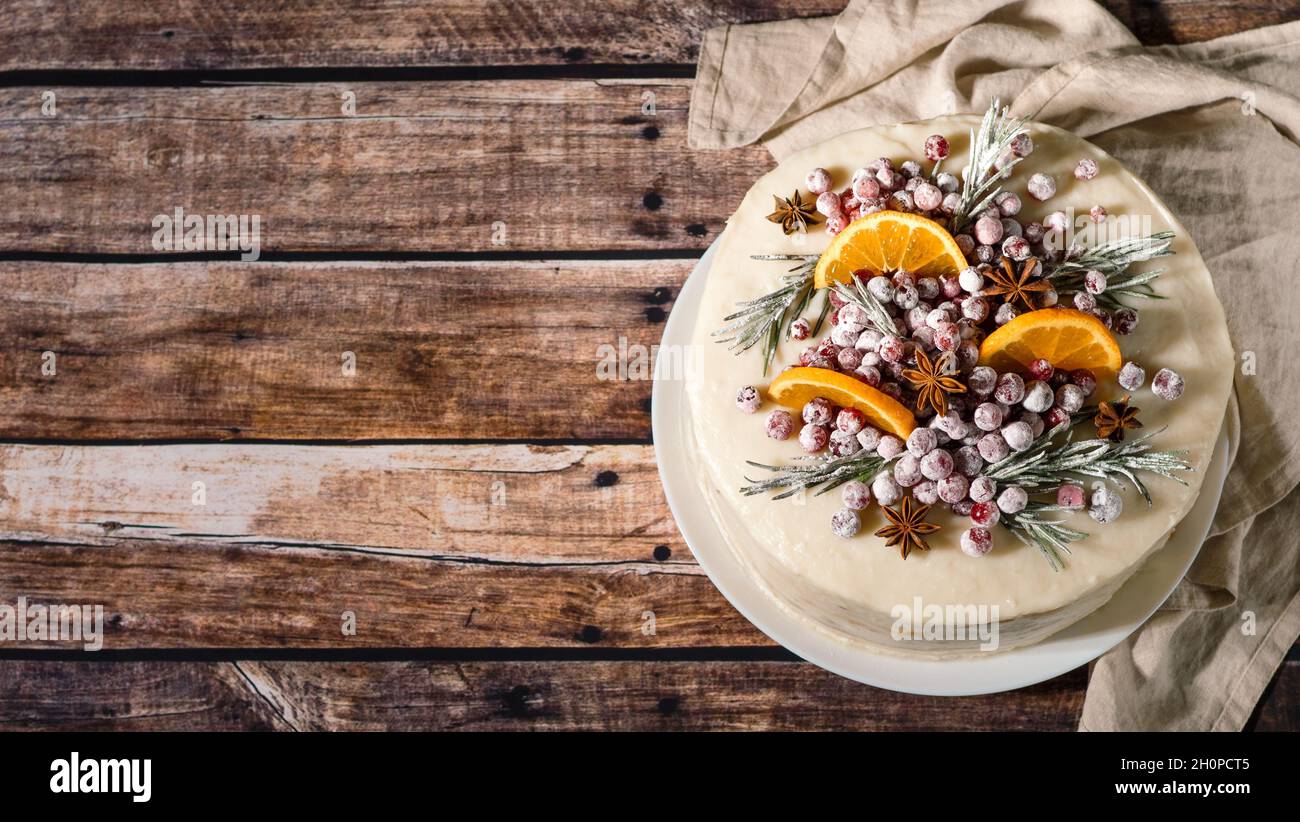 Winter hausgemachter Kuchen auf Holzhintergrund. Weisse Sahnetorte mit Rosmarin, Preiselbeeren, Sternanise und Orangen in Scheiben. Speicherplatz kopieren. Draufsicht Stockfoto