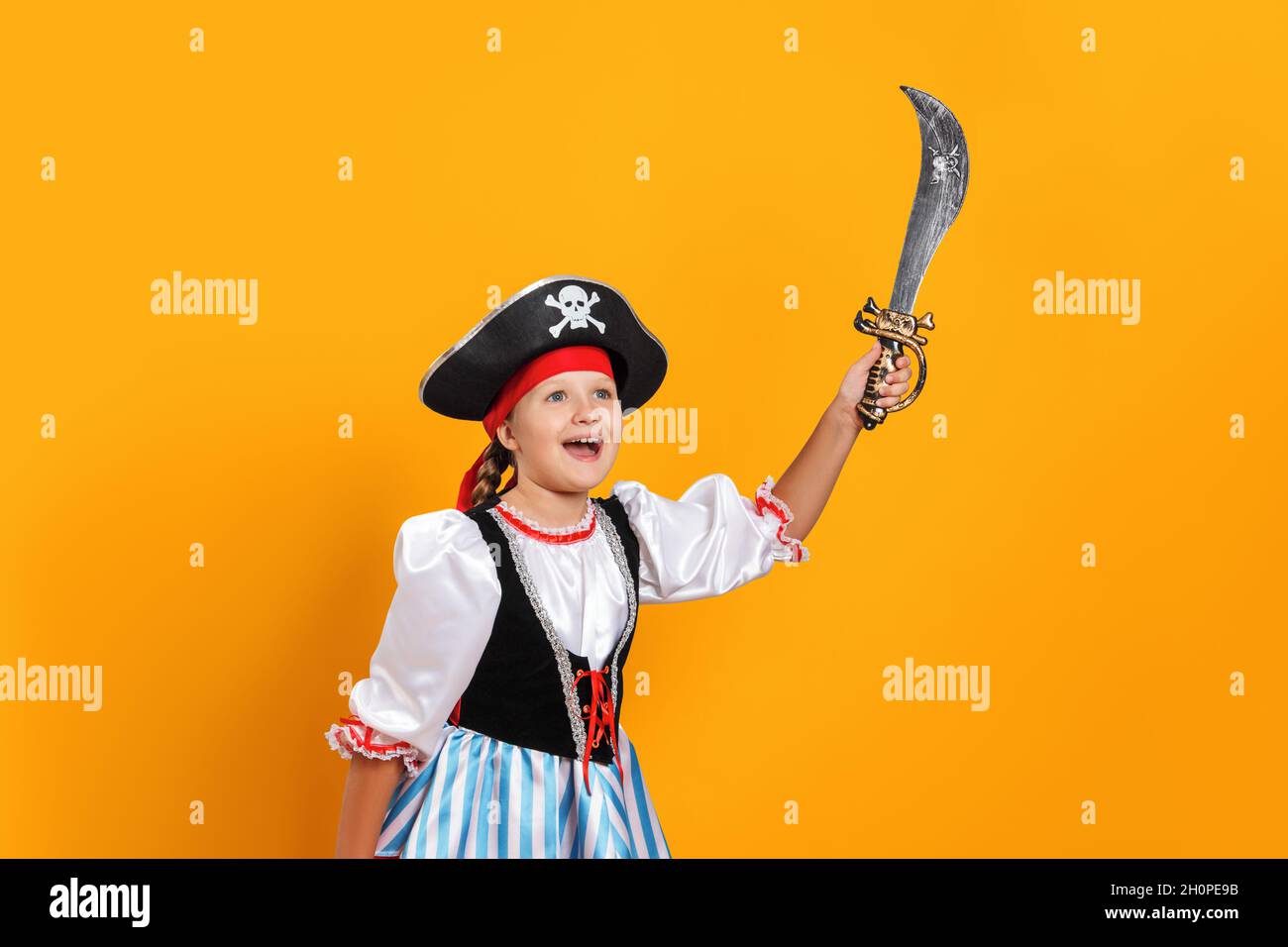 Halloween. Fröhliches kleines Mädchen in einem Karnevalskostüm eines Piraten im Studio auf einem farbigen gelben Hintergrund. Das Kind hält einen Säbel. Stockfoto