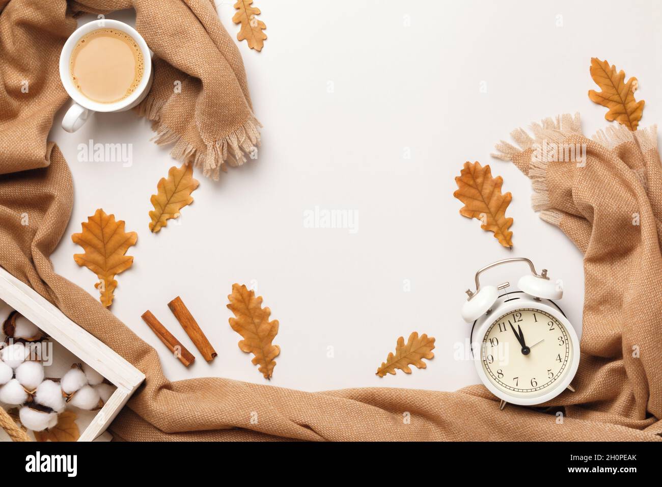 Herbstliches Gemütlichkeit-Konzept. Beigefarbener Kaschmir-Schal mit Kaffeebecher-Wecker mit herbstlichen Eichenlaub auf hellgrauem Hintergrund. Flach, oben liegend, Kopieplatz Stockfoto