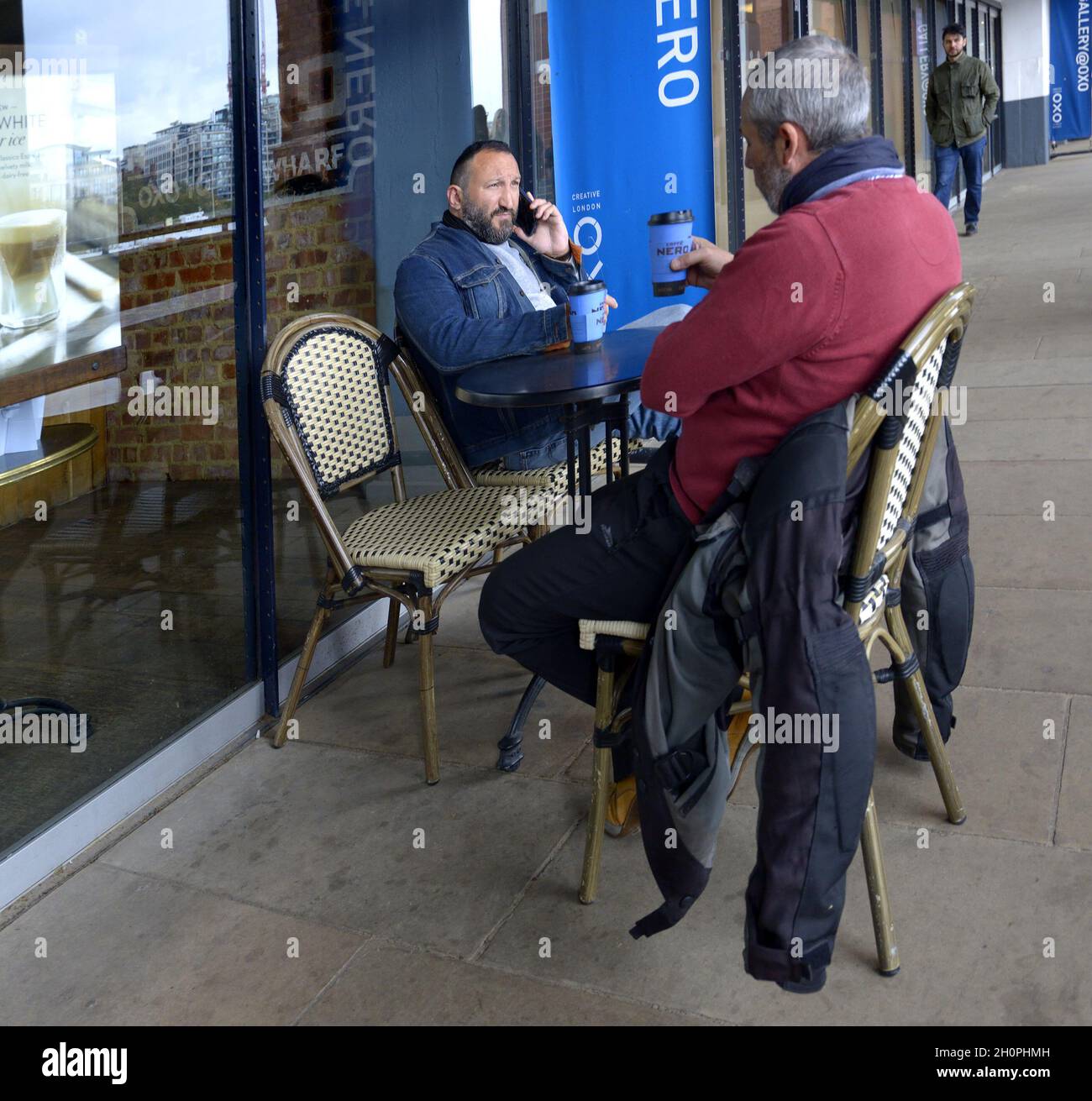 London, England, Großbritannien. Männer, die vor einem Café mit Kaffee und Handy sitzen Stockfoto