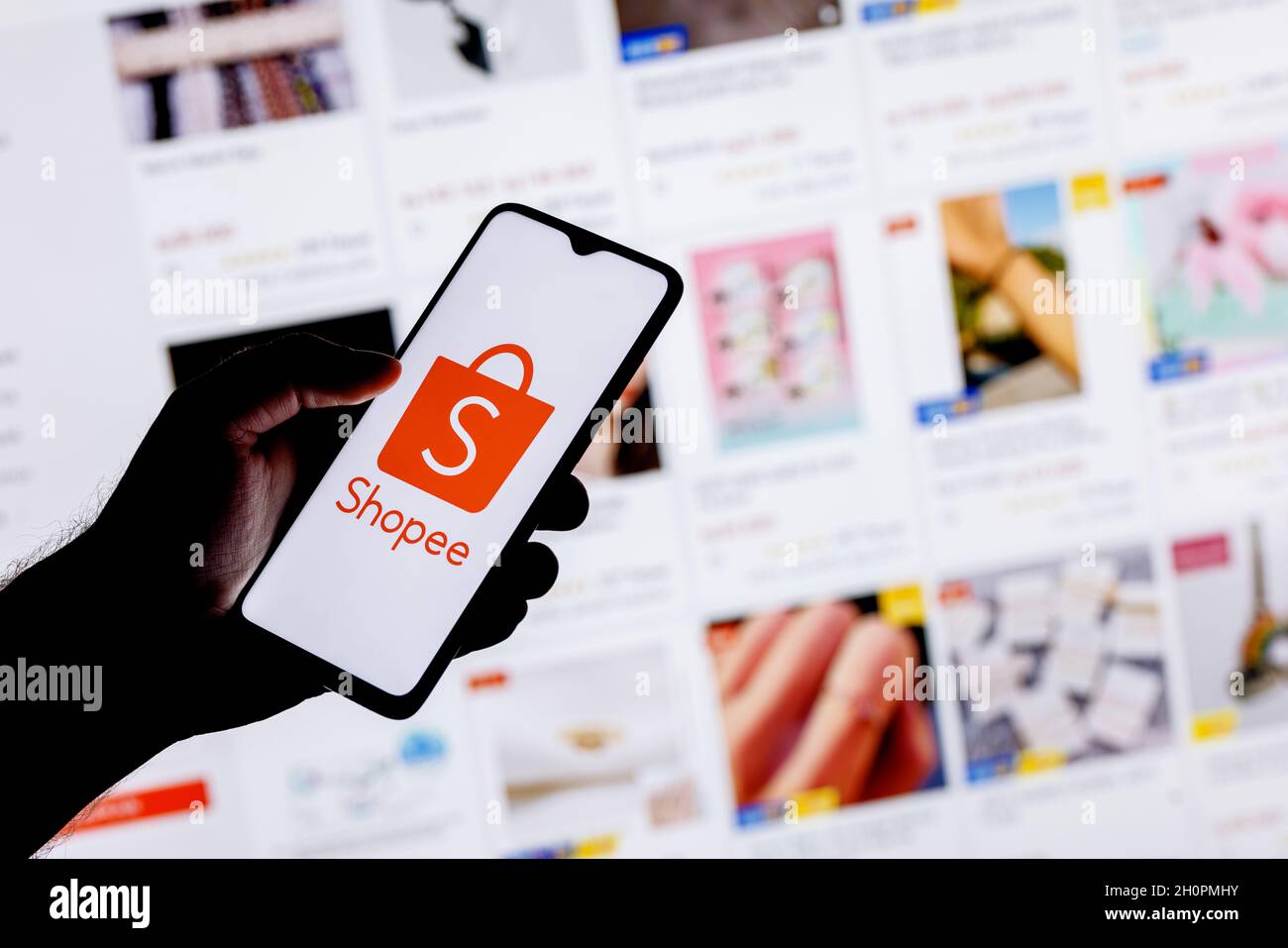 Shopee ist ein E-Commerce-Technologieunternehmen. Ein Smartphone mit dem Shopee-Logo in einer Hand auf dem Hintergrund des Katalogs von der Website. Stockfoto