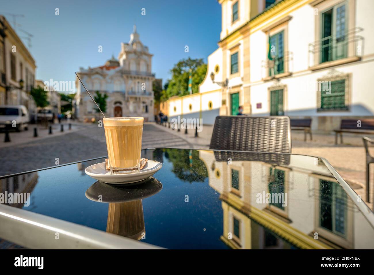 Kaffee mit Milch namens galao mit Wahrzeichen der Belmarco-Villa im Hintergrund, Faro, Algarve, Portugal Stockfoto