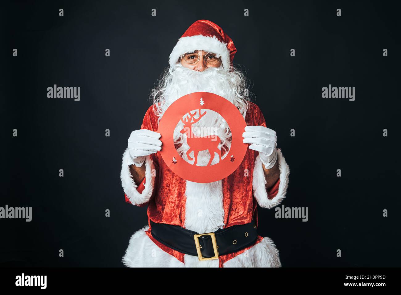 Mann, der als Weihnachtsmann gekleidet ist und ein Verkehrsschild mit einem verbietenden Rentier auf schwarzem Hintergrund hält. Weihnachtskonzept, Weihnachtsmann, Geschenke, Feier. Stockfoto
