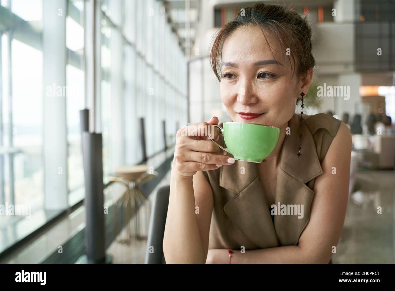 Reife asiatische Frau trinkt Tee im modernen Hotelrestaurant Stockfoto