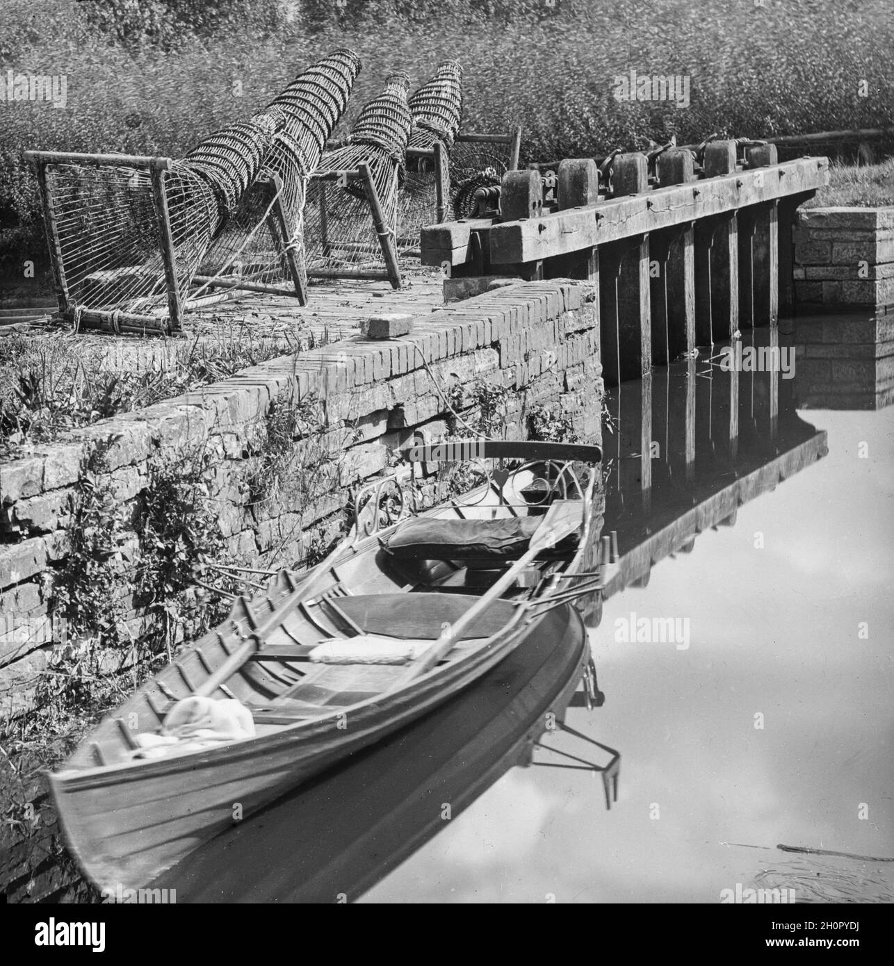 Vintage viktorianisches Schwarz-Weiß-Foto zeigt traditionelle englische Fischfallen an der Seite eines Flusses mit einem kleinen Ruderboot. Stockfoto