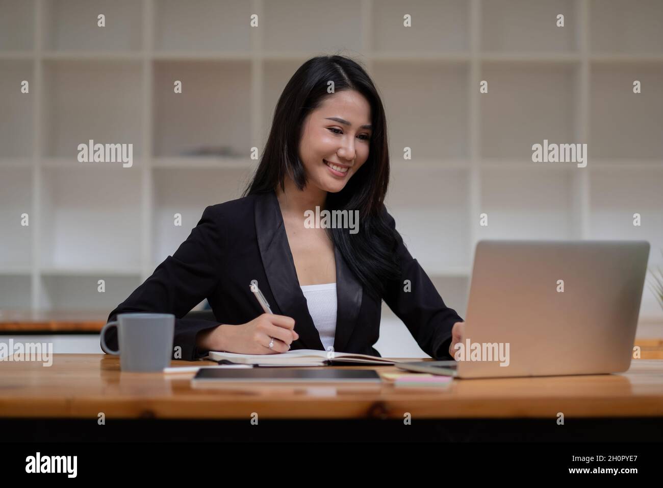 Asiatische Geschäftsfrau arbeitet am Laptop-Computer während der Notizen im Büro. Online-Meeting Webinar-Konzept. Stockfoto