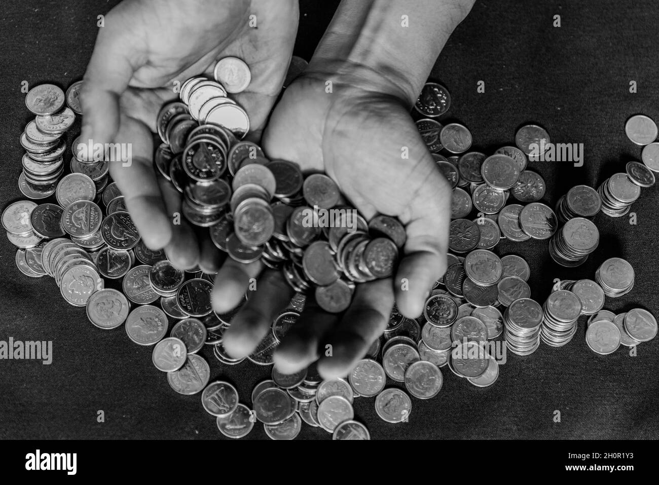 Graustufenaufnahme der Hände eines Mannes mit zahlreichen Münzen Stockfoto