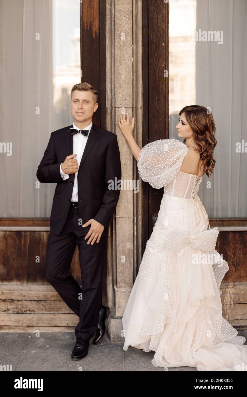 Foto von Braut und Bräutigam, die miteinander reden und sich vor dem Hintergrund der Türen anschauen. Eingang zum Gebäude. Hochzeitskleid, Anzug. W Stockfoto