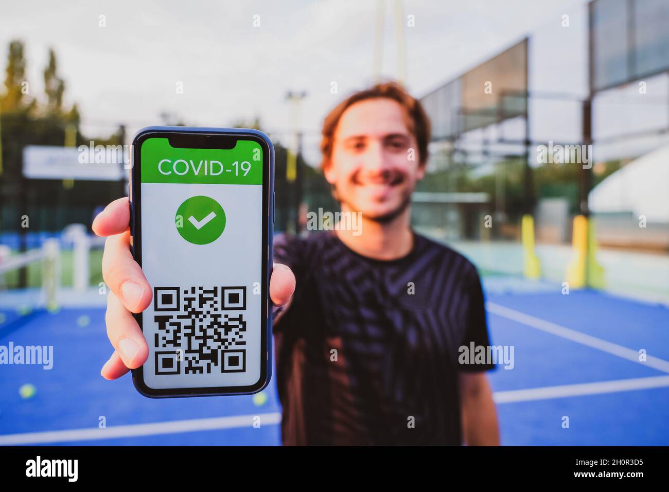 Junger Mann zeigt Impfpass covid-19 mit App auf Smartphone erster Sport, Coronavirus-Konzept Stockfoto
