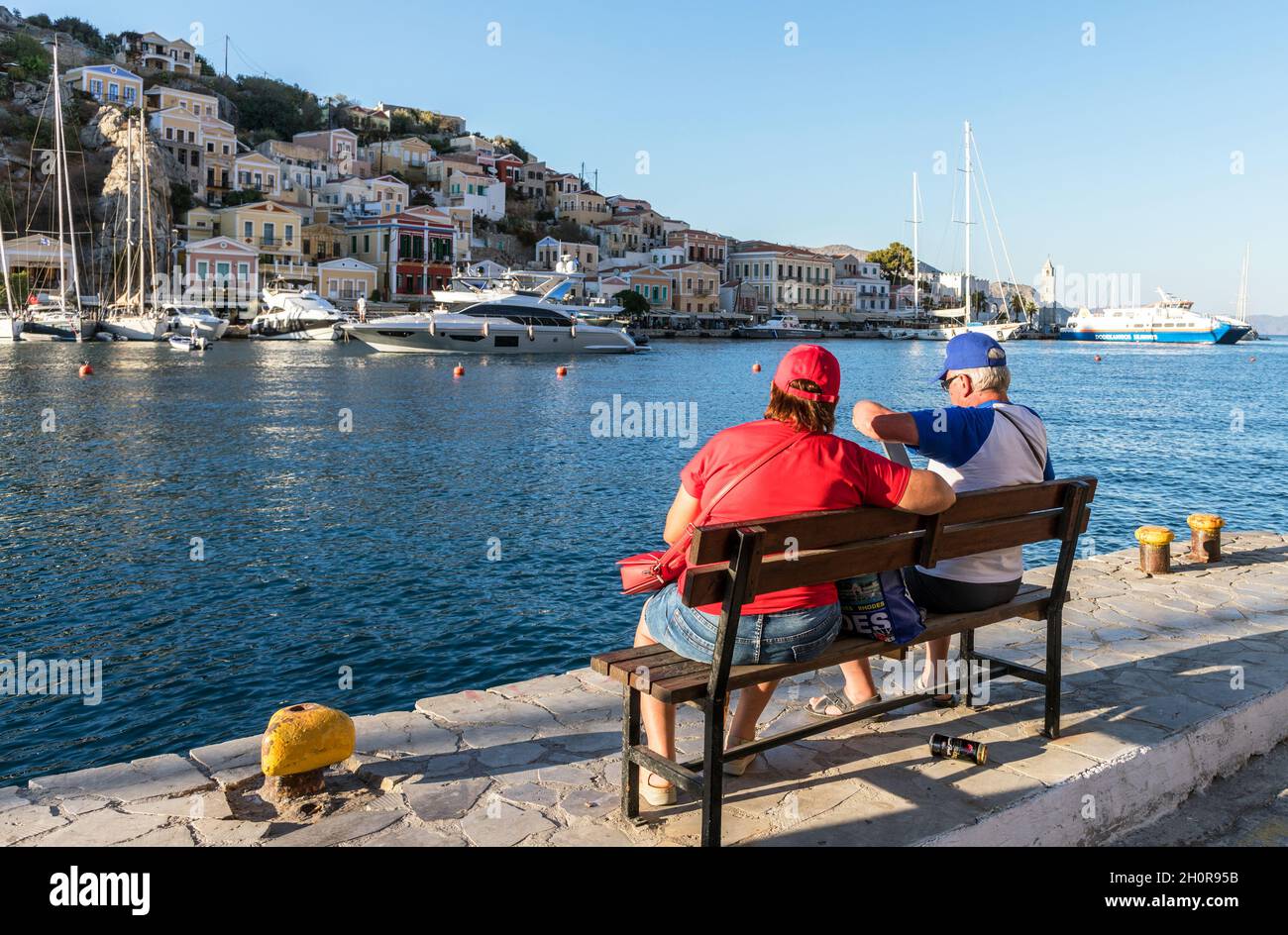 Touristen, die an der Hafenmauer auf den griechischen Symi-Inseln sitzen Stockfoto