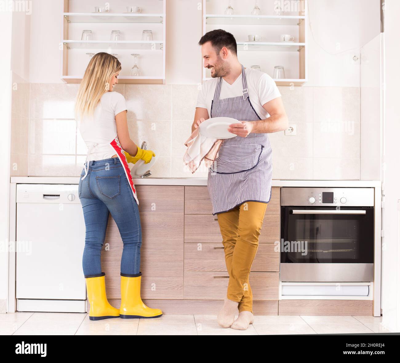 Glückliches junges Paar, das in der Küche Geschirr wascht und abwischt Stockfoto