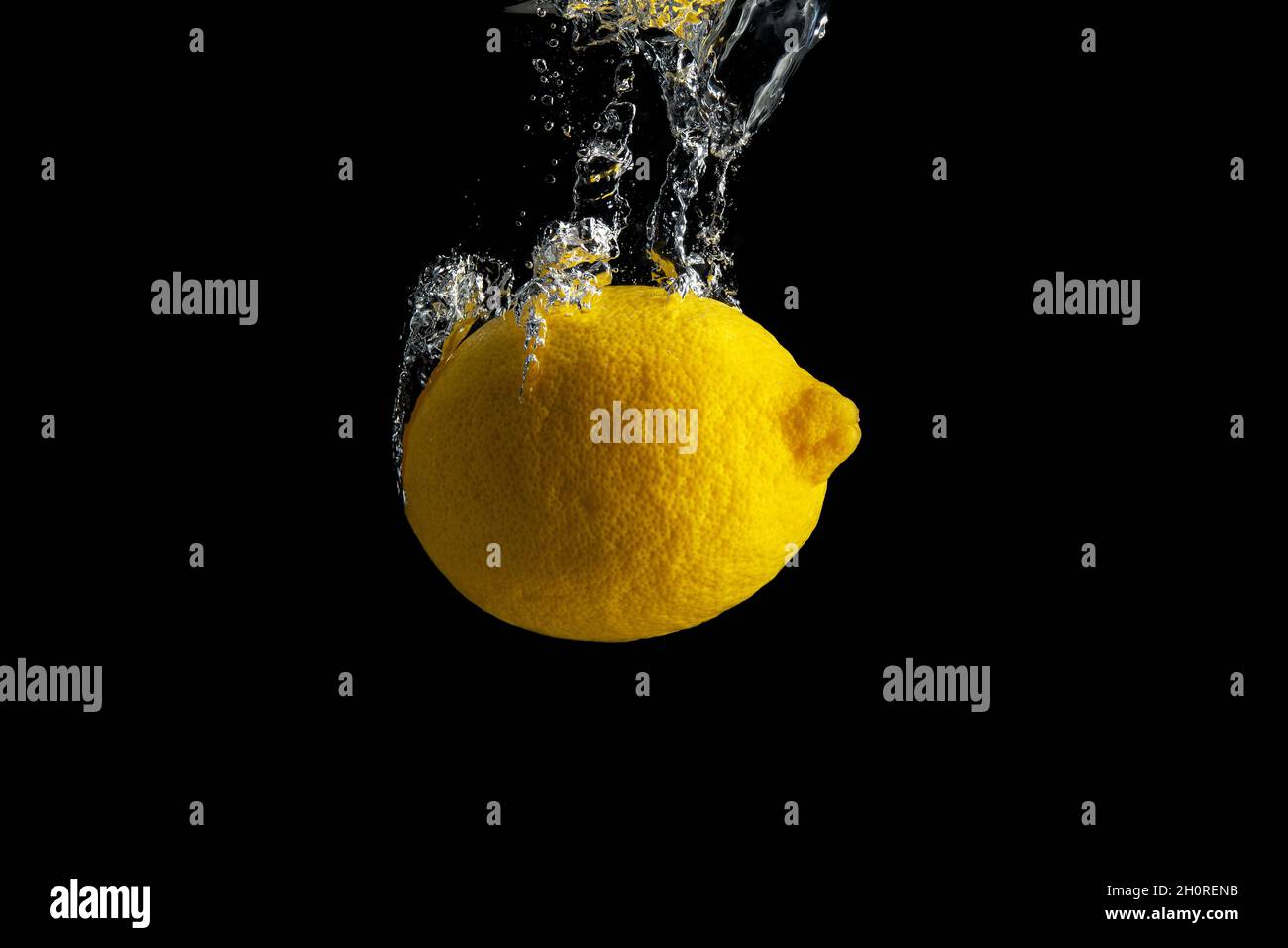 Frische gelbe Zitrone im Wasser Spritzer isoliert auf schwarzem Hintergrund. Minimales Lebensmittelkonzept. Stockfoto