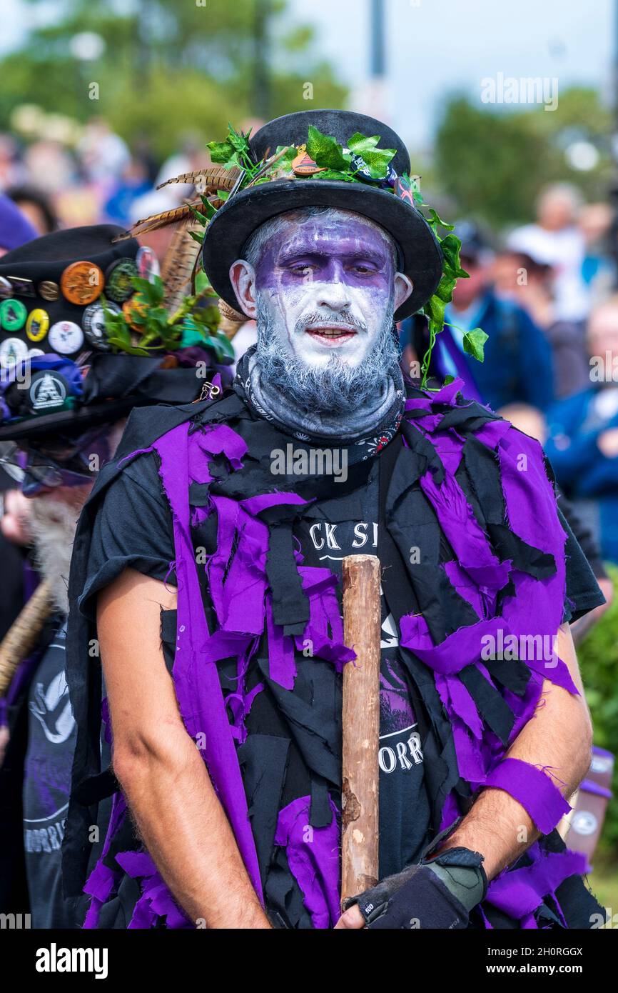 Nahaufnahme der halblangen Volkstänzerin mit Bart von den Black Swam Morris Tänzern. Lila und weiß gemaltes Gesicht, hält Personal, gegenüber dem Betrachter. Stockfoto