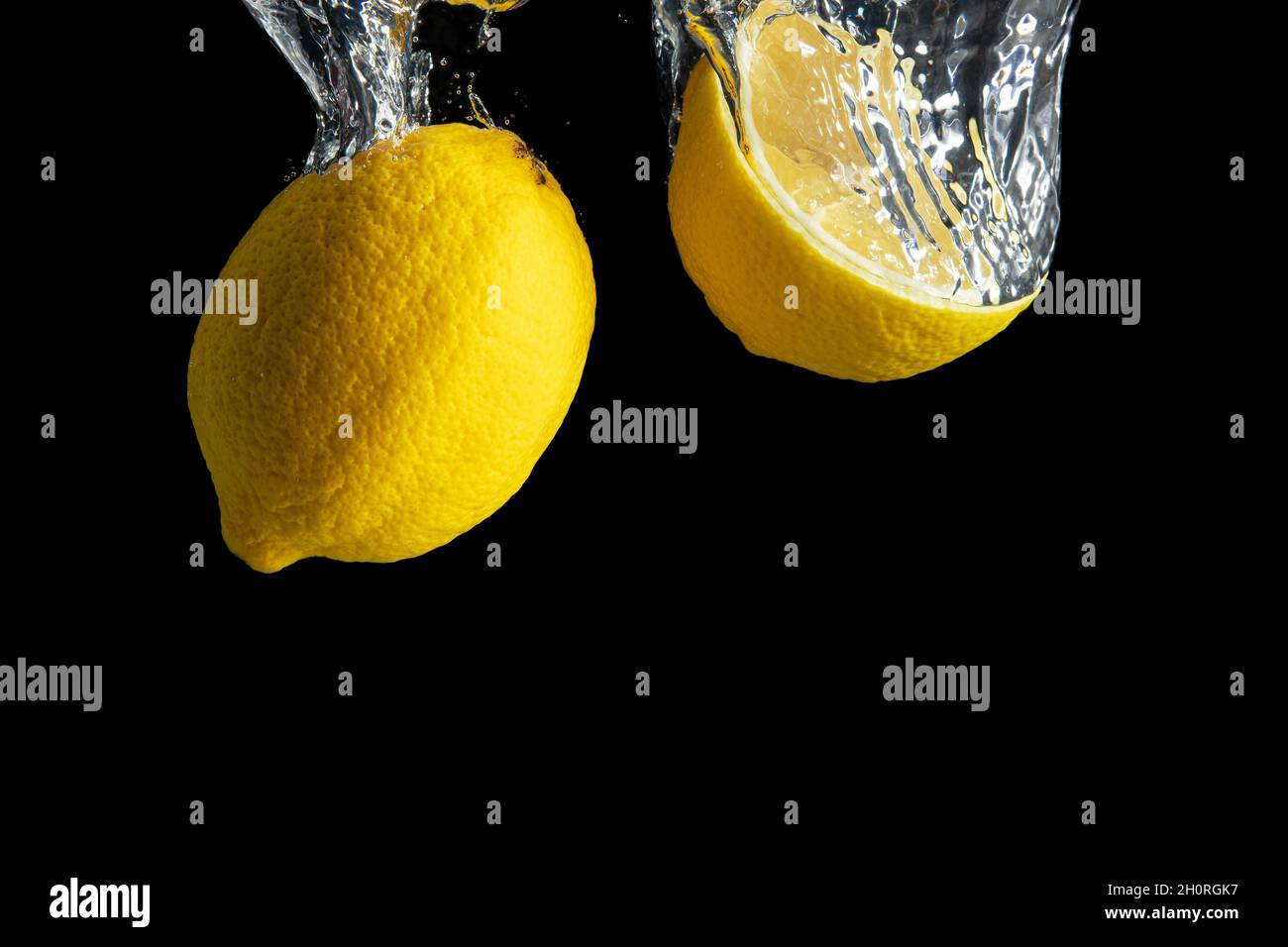Frische gelbe Zitrone im Wasser Spritzer isoliert auf schwarzem Hintergrund. Minimales Lebensmittelkonzept. Stockfoto