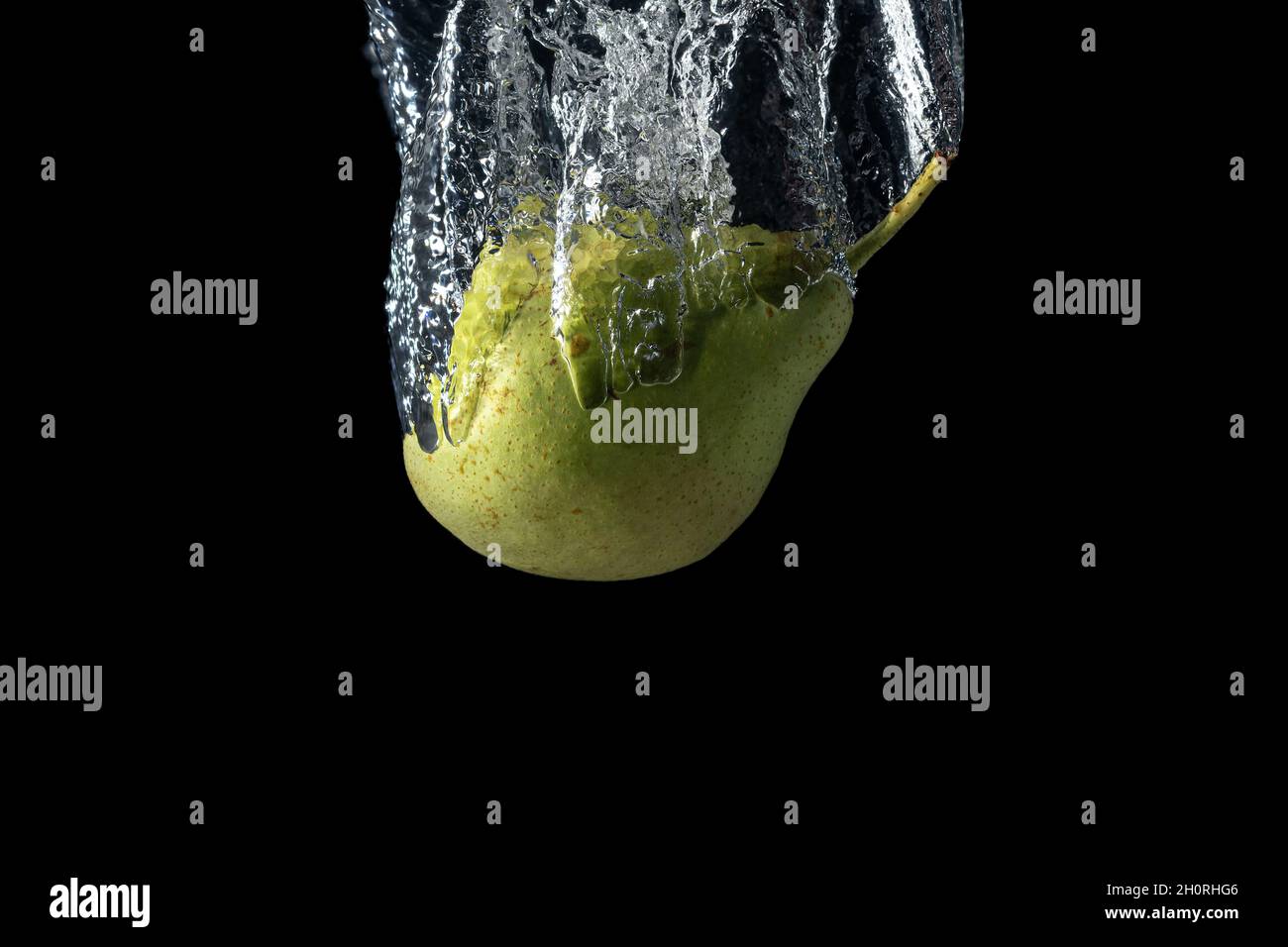 Frische grüne Birne im Wasser spritzt isoliert auf schwarzem Hintergrund. Minimales Lebensmittelkonzept. Stockfoto