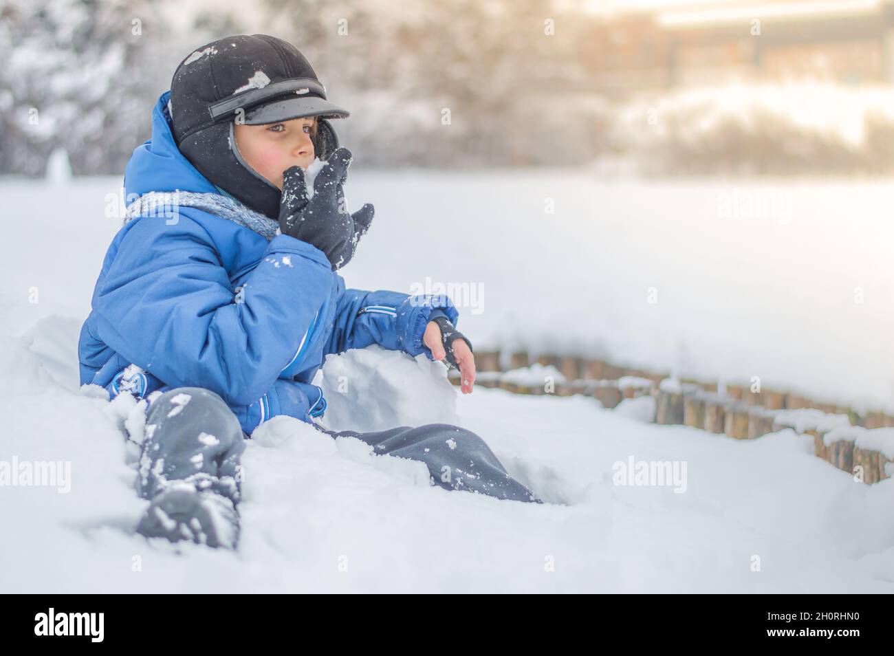 Ein glücklicher Junge spielt Schneebälle und frisst Schnee auf einer verschneiten Lichtung. Stockfoto