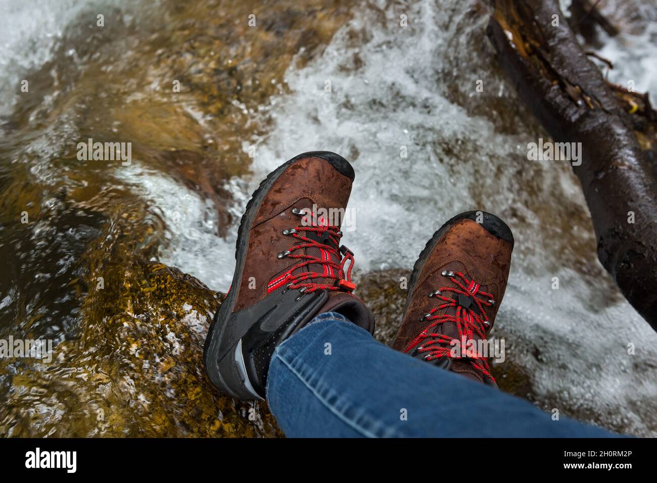 Damenfüße in Trekkingstiefeln auf nassen Flusssteinen Stockfoto