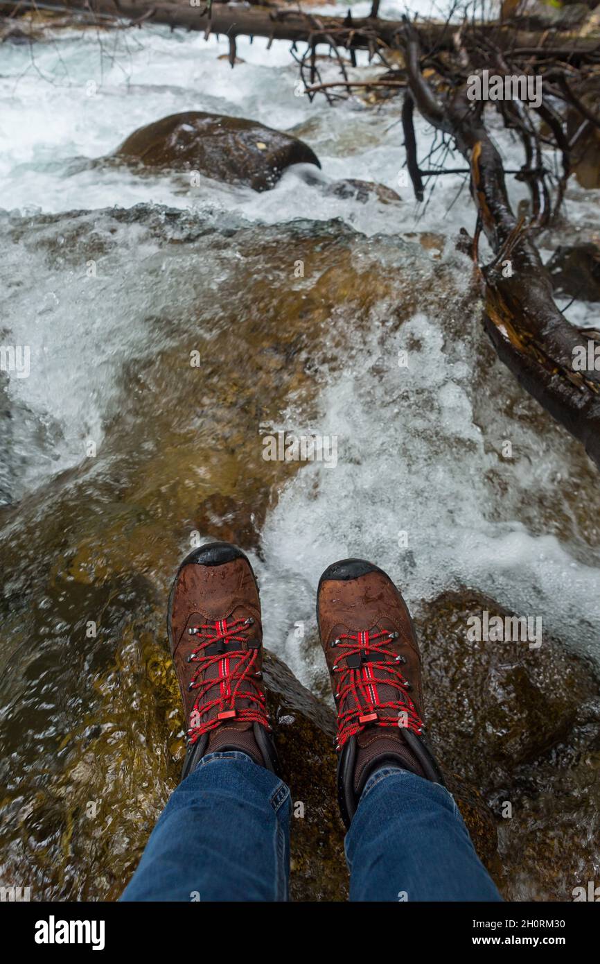 Damenfüße in Trekkingstiefeln auf nassen Flusssteinen Stockfoto